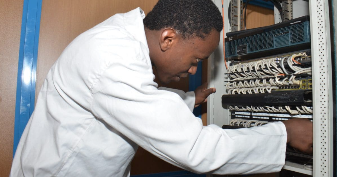 A technician working on a server rack in a data center, wearing a white lab coat.
