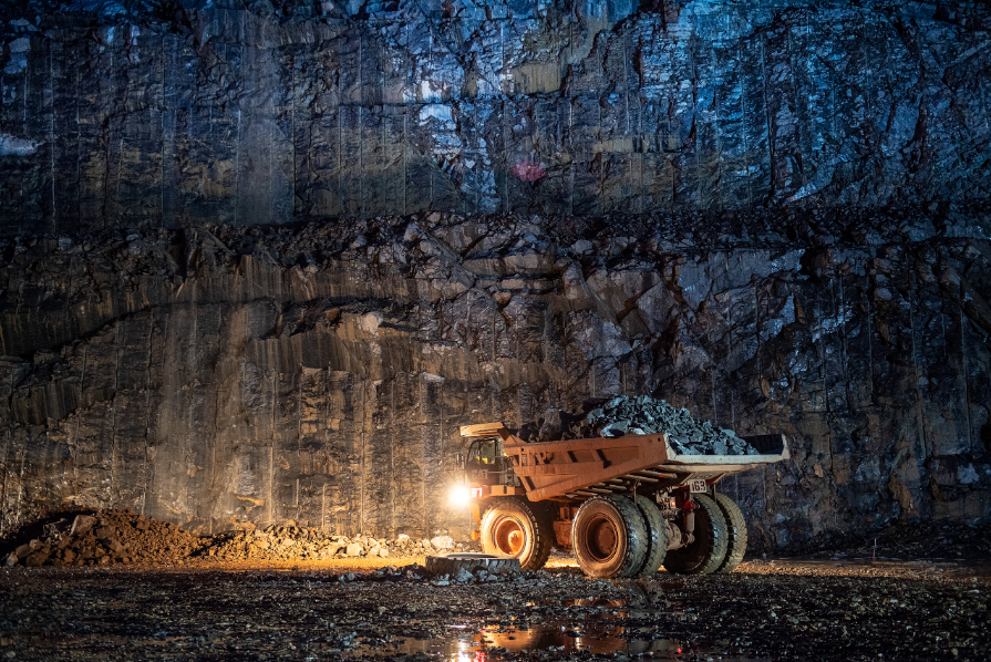 A large mining dump truck carrying rocks inside an underground quarry with a rocky wall background.