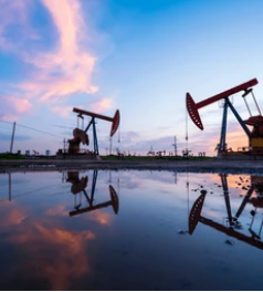 Oil pumps in an oil field during sunset, reflected in a large puddle of water.