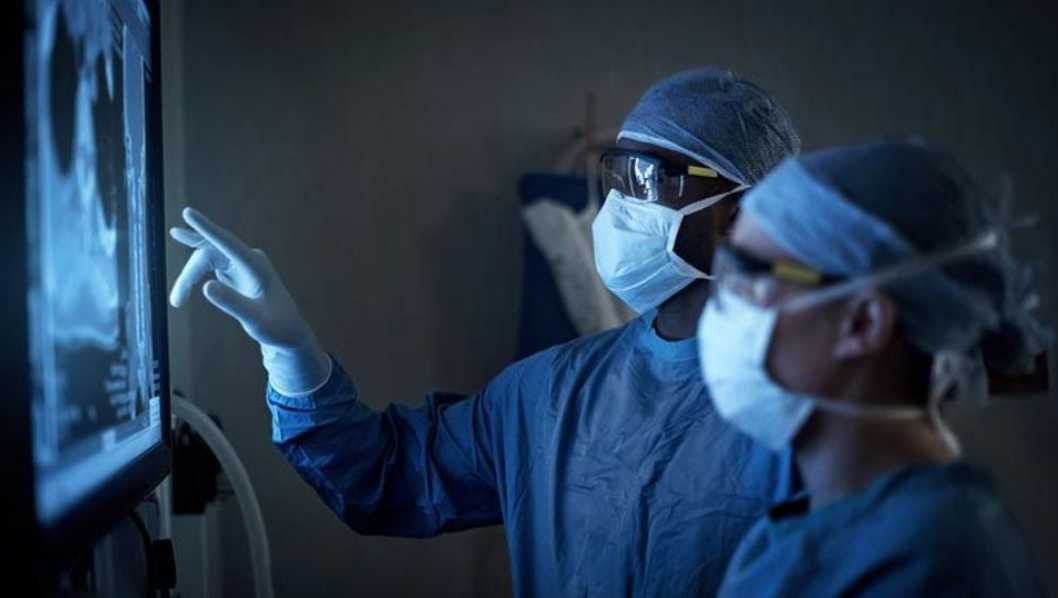 Two healthcare professionals with medical specialisation in South Africa in protective gear looking at medical images on a monitor.