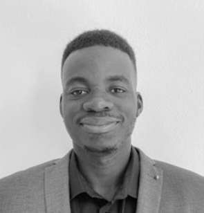 A smiling young man wearing a dark shirt and blazer against a plain background.
