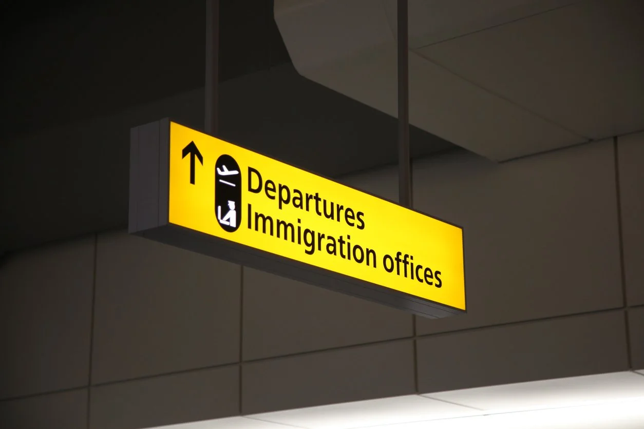 Airport signage indicating directions to departures and immigration offices, with an upward arrow and a suitcase icon.
