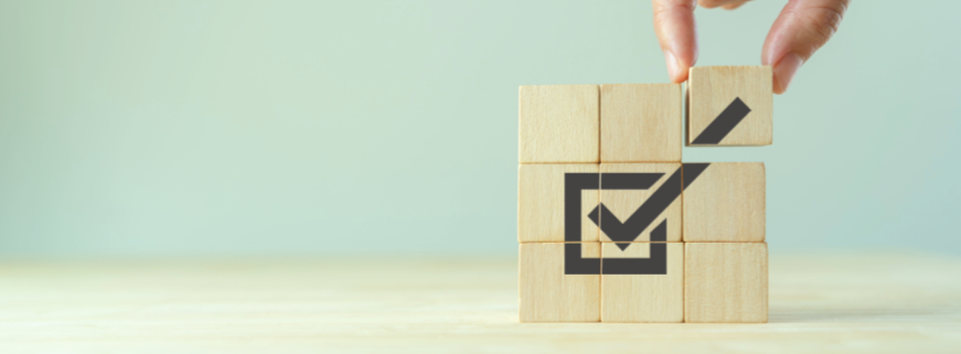 A hand arranging wooden blocks with a checkmark inside a square drawn on the blocks.