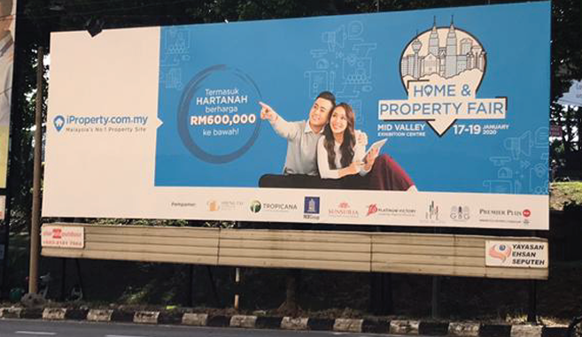 Billboard advertising the Home & Property Fair at Mid Valley Exhibition Centre from January 17-19, 2020, with a couple smiling and pointing, featuring contact information and logos of sponsors.
