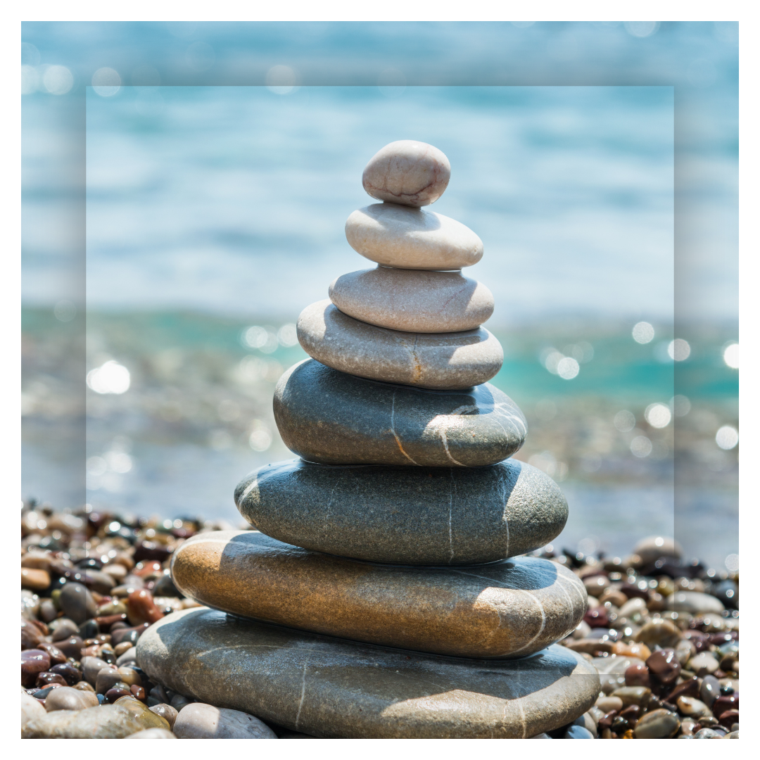 Stacked smooth stones on a pebble beach with ocean waves and bokeh background.