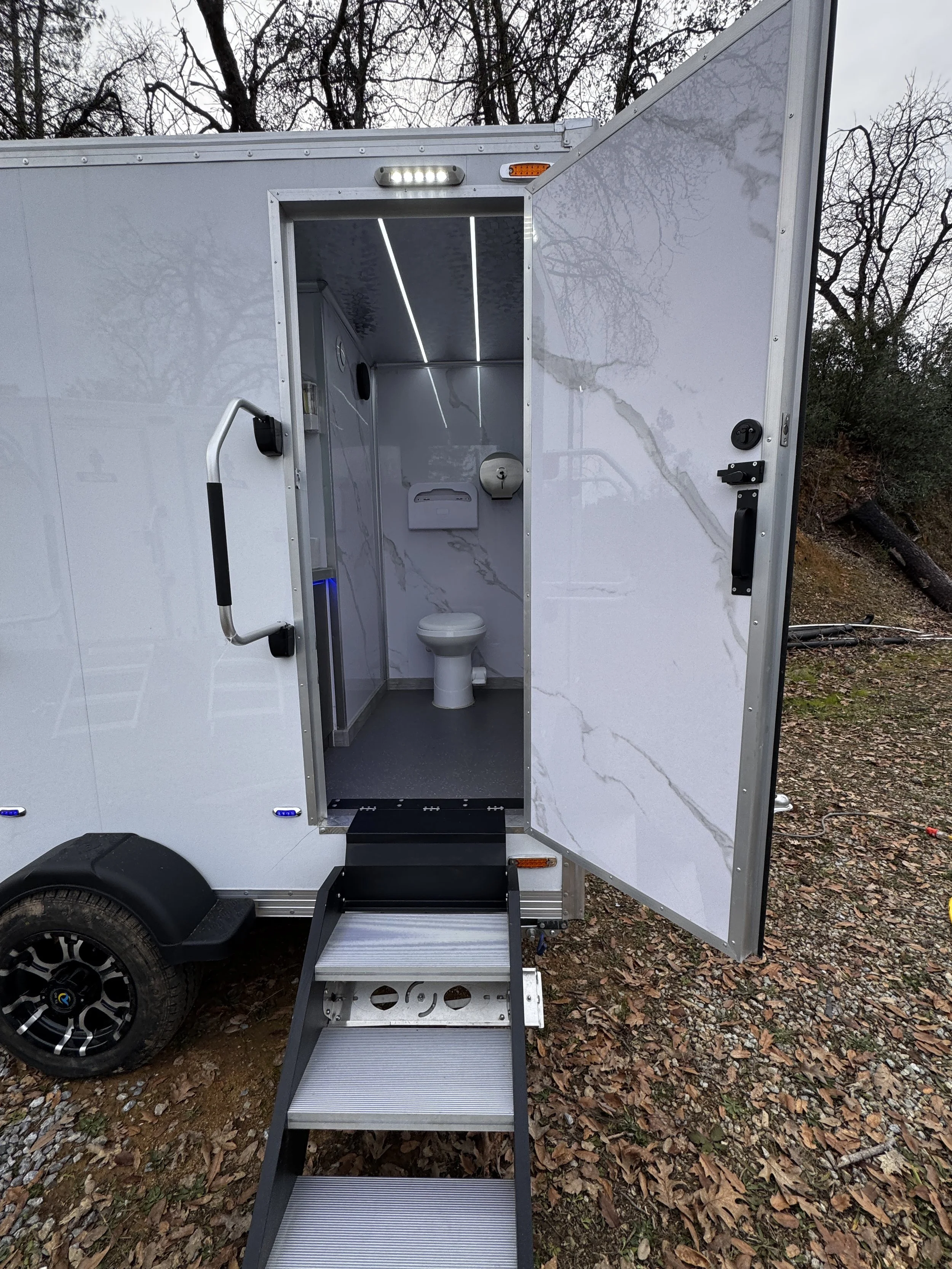 Mobile restroom trailer with open door, steps leading inside, and toilet visible.