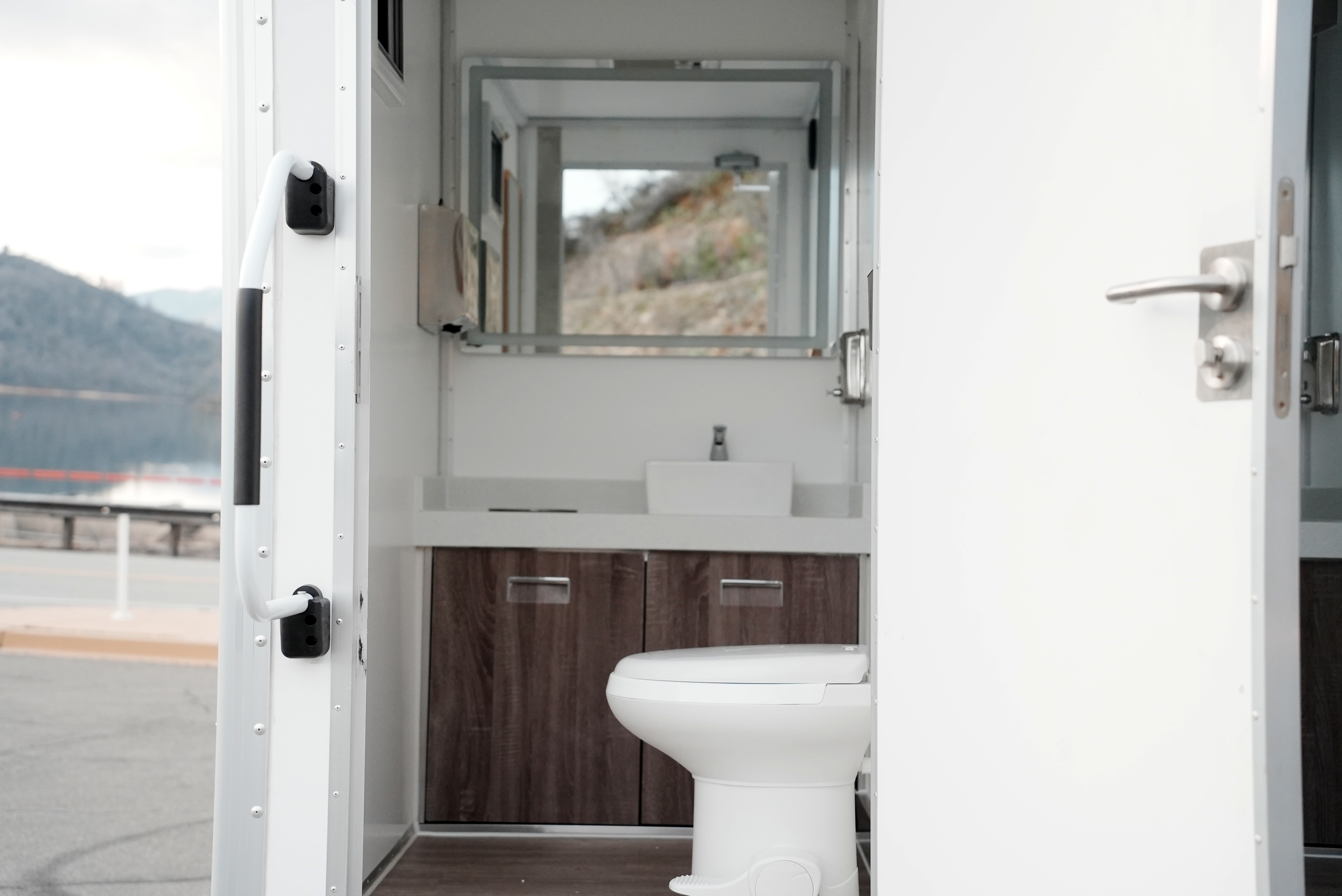 Interior of a portable restroom with toilet, sink, and mirror.