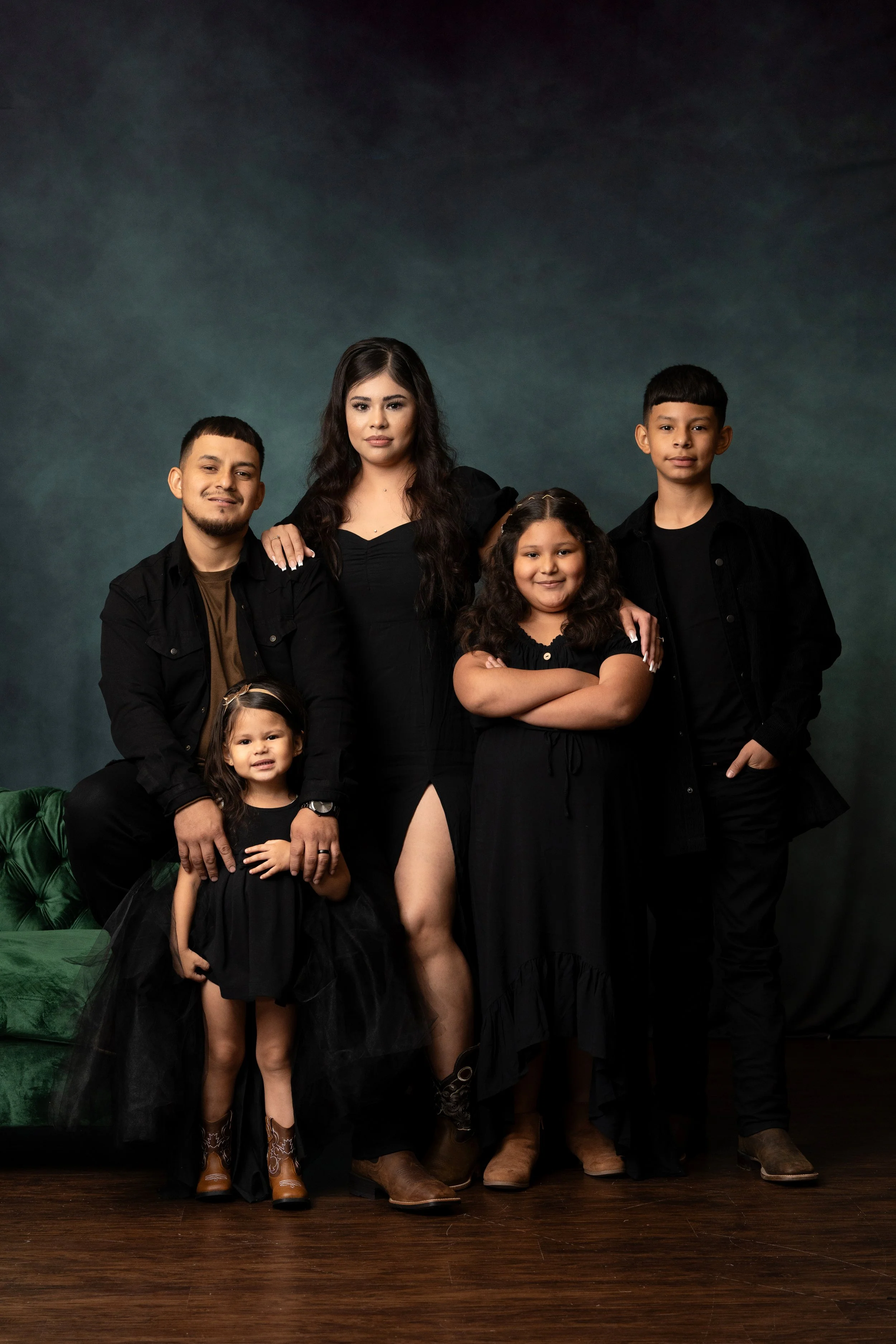 A family portrait of six people, three adults and three children, dressed in black and cowboy boots, standing in front of a dark teal background. Omaha Family portrait photographer.  Located in Gretna, NE