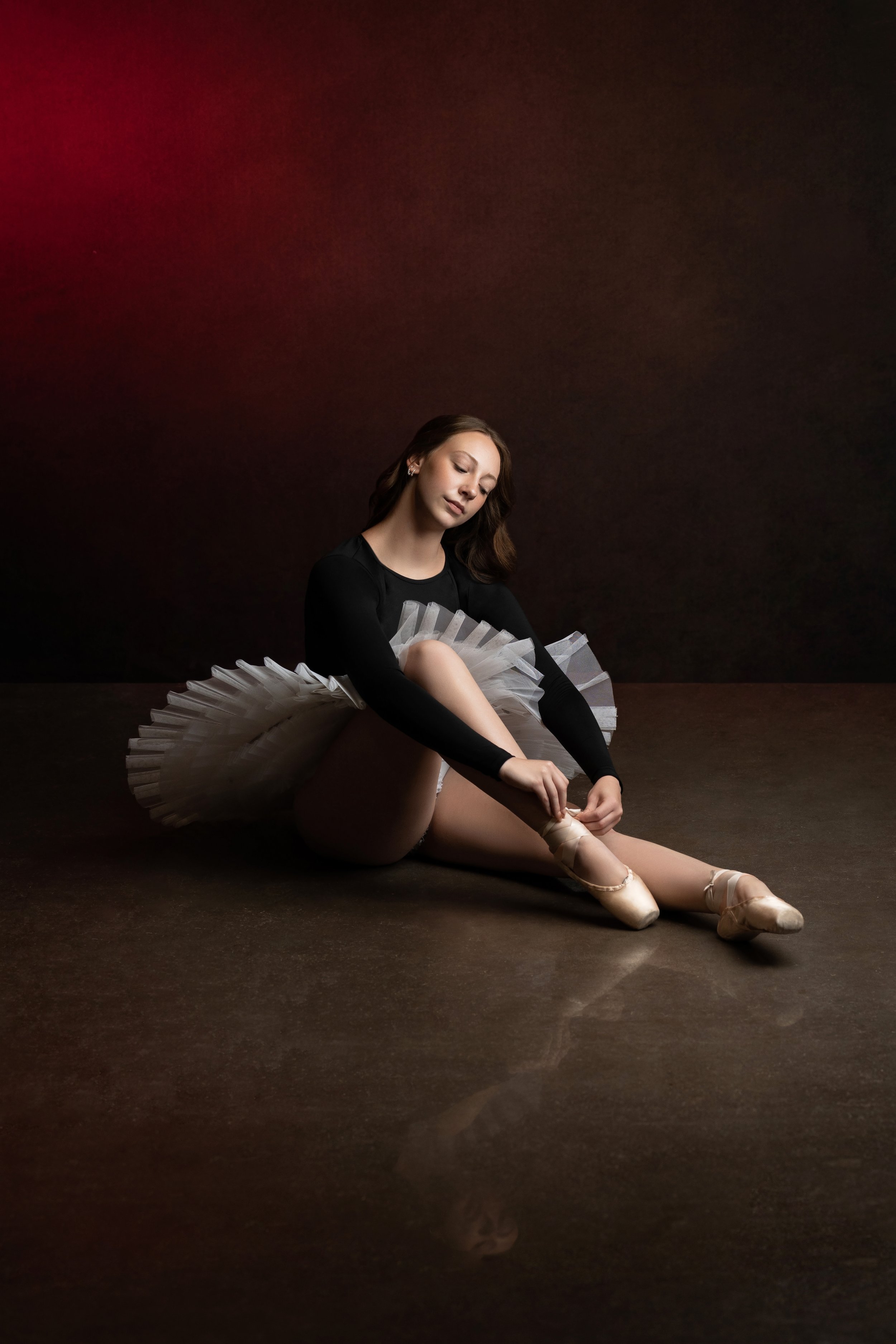 A ballerina in a tutu sits and ties her point shoes at her art of dance session