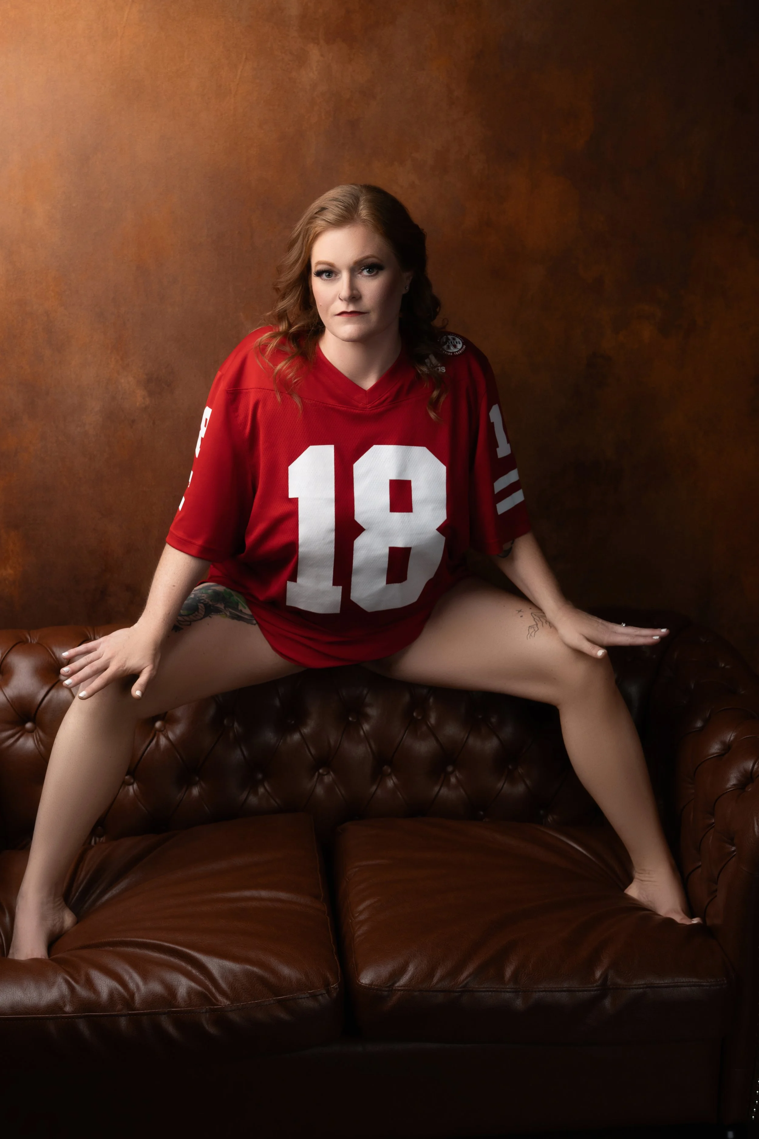 A redhead wearing a jersey strikes a p[owerful pose on a leather sofa