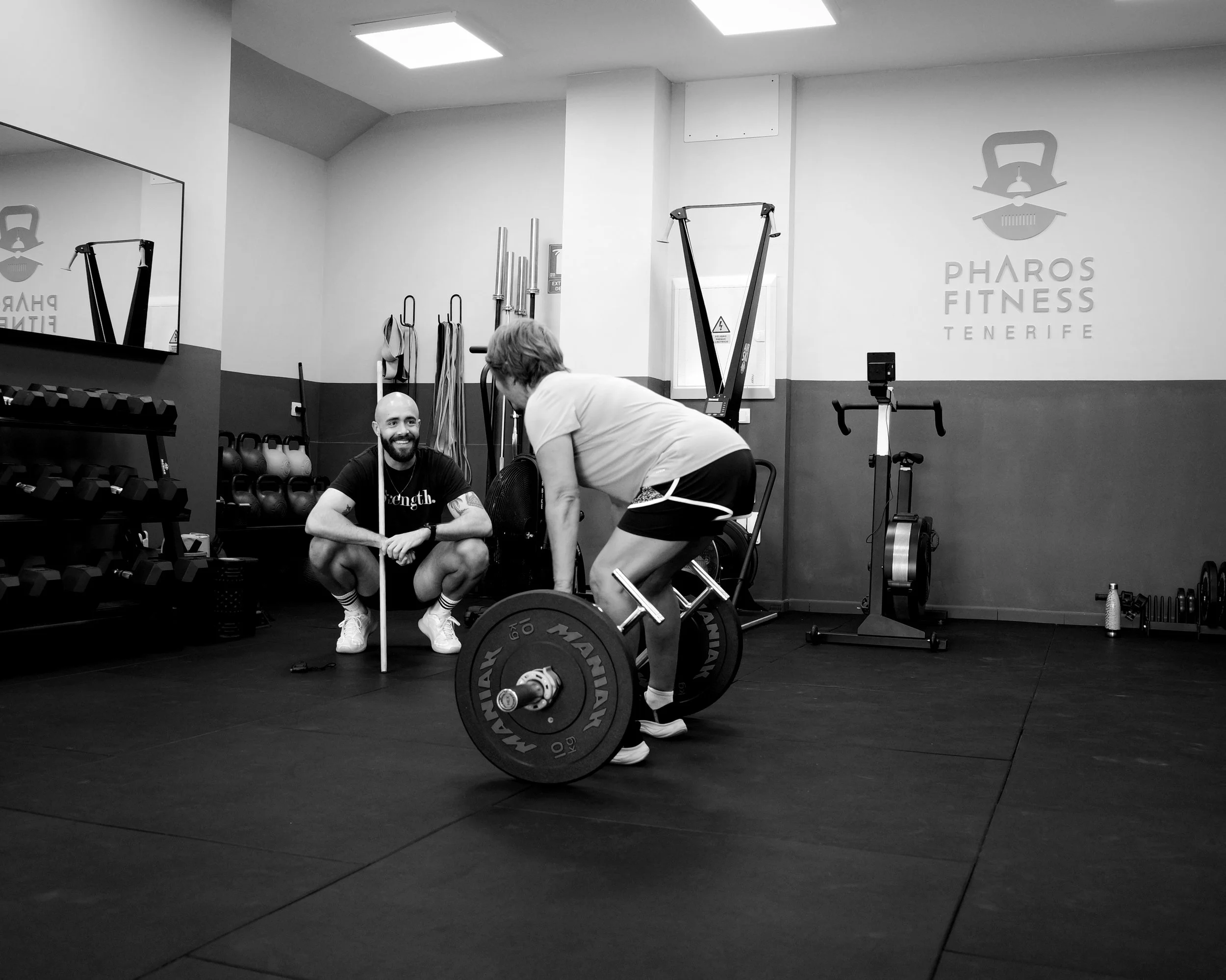 A man performing a leg exercise with a coach assisting him in a gym, surrounded by weightlifting equipment.