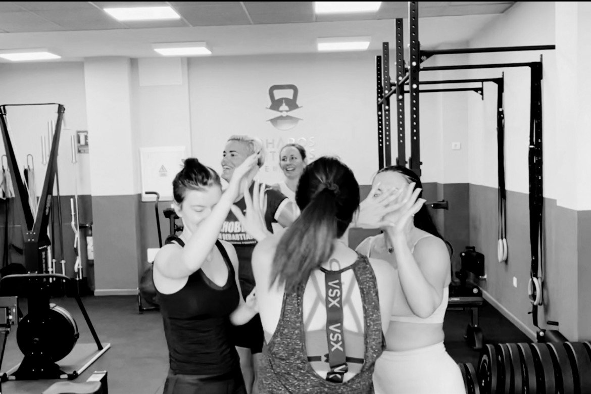 Group of women and a man celebrating in a gym, with gym equipment visible in the background.