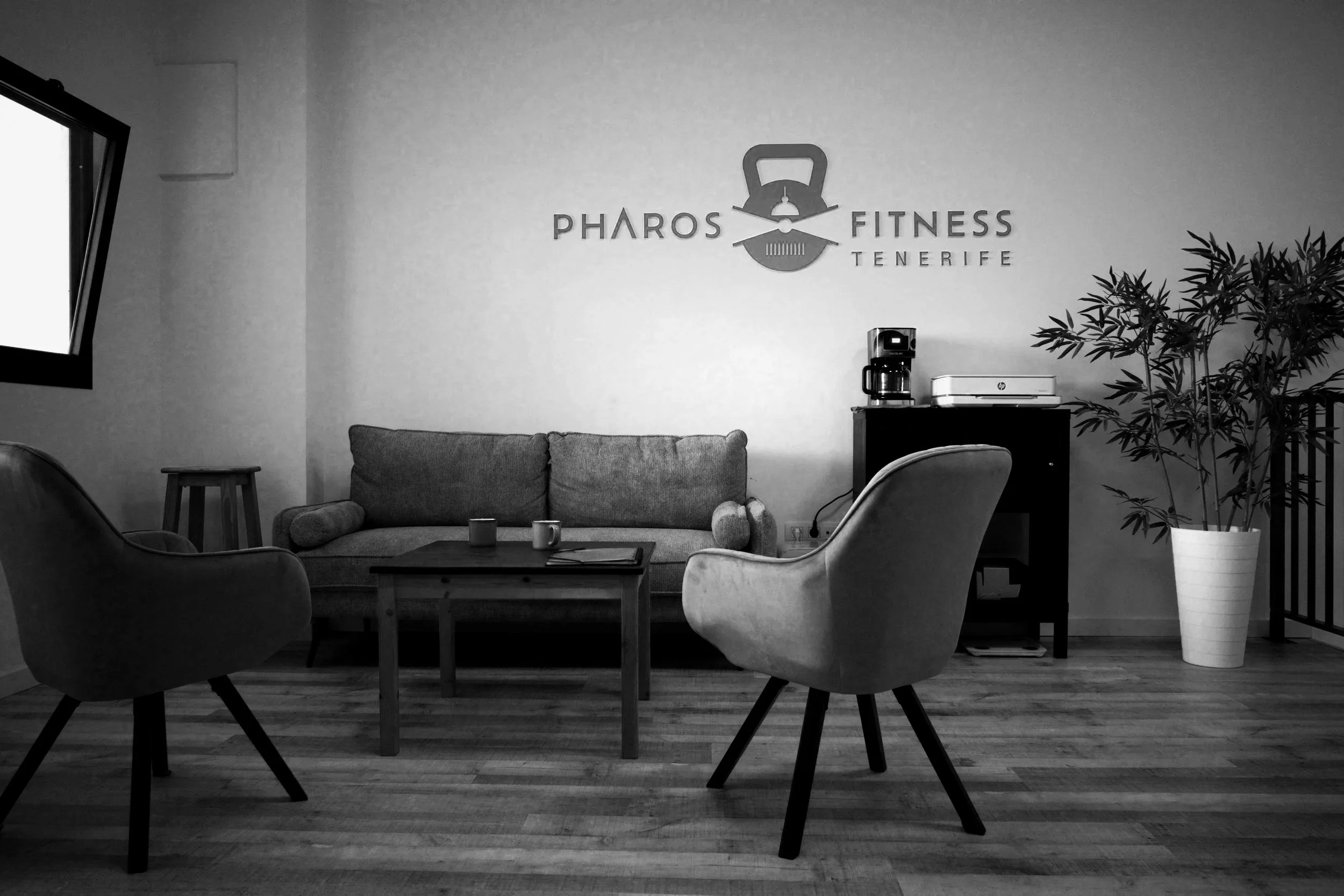 A waiting area at Pharos Fitness in Tenerife with a sofa, two armchairs, coffee table, and potted plant.