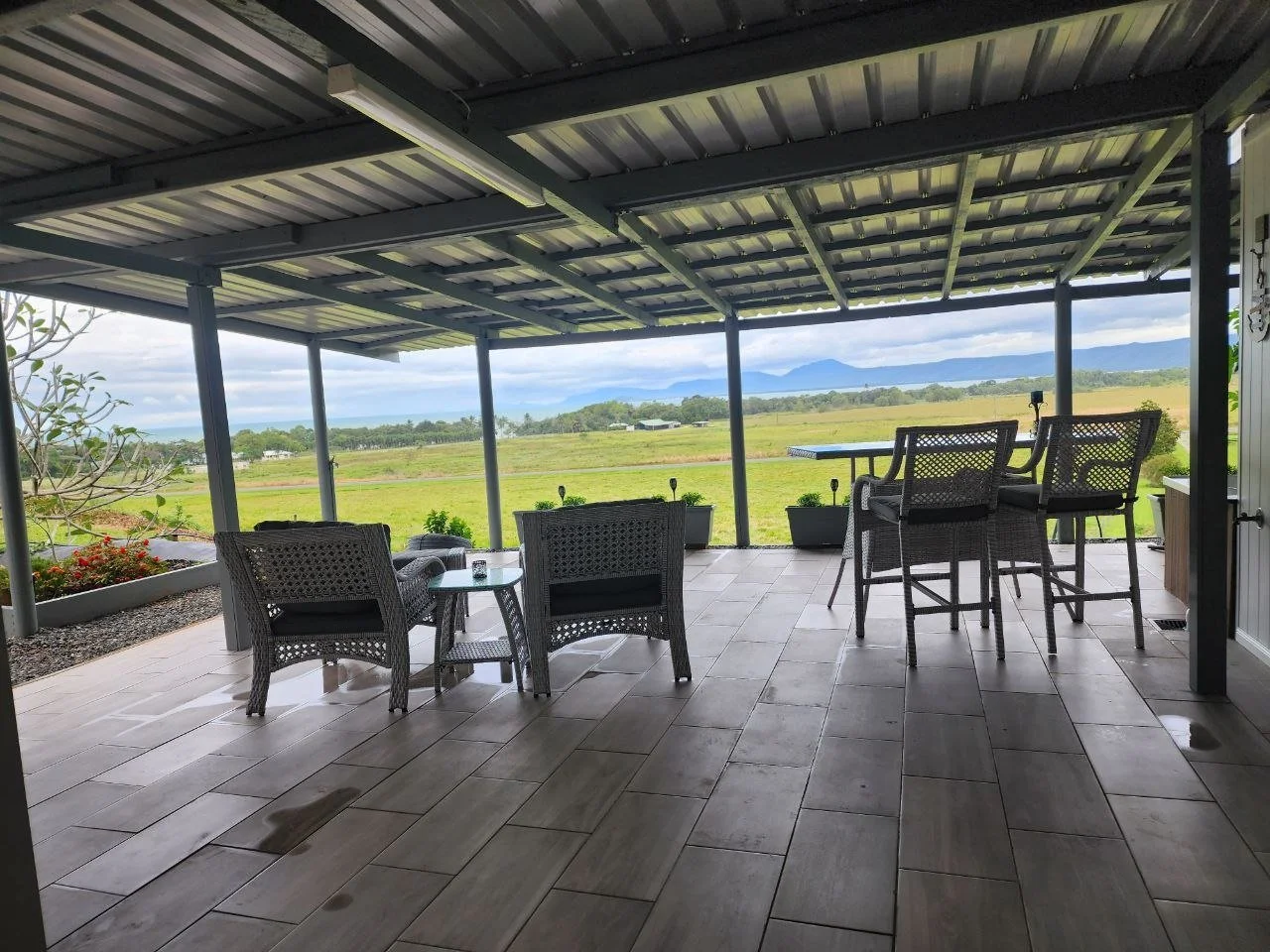 Covered outdoor patio with wicker chairs, a high table, and a view of open fields and distant mountains