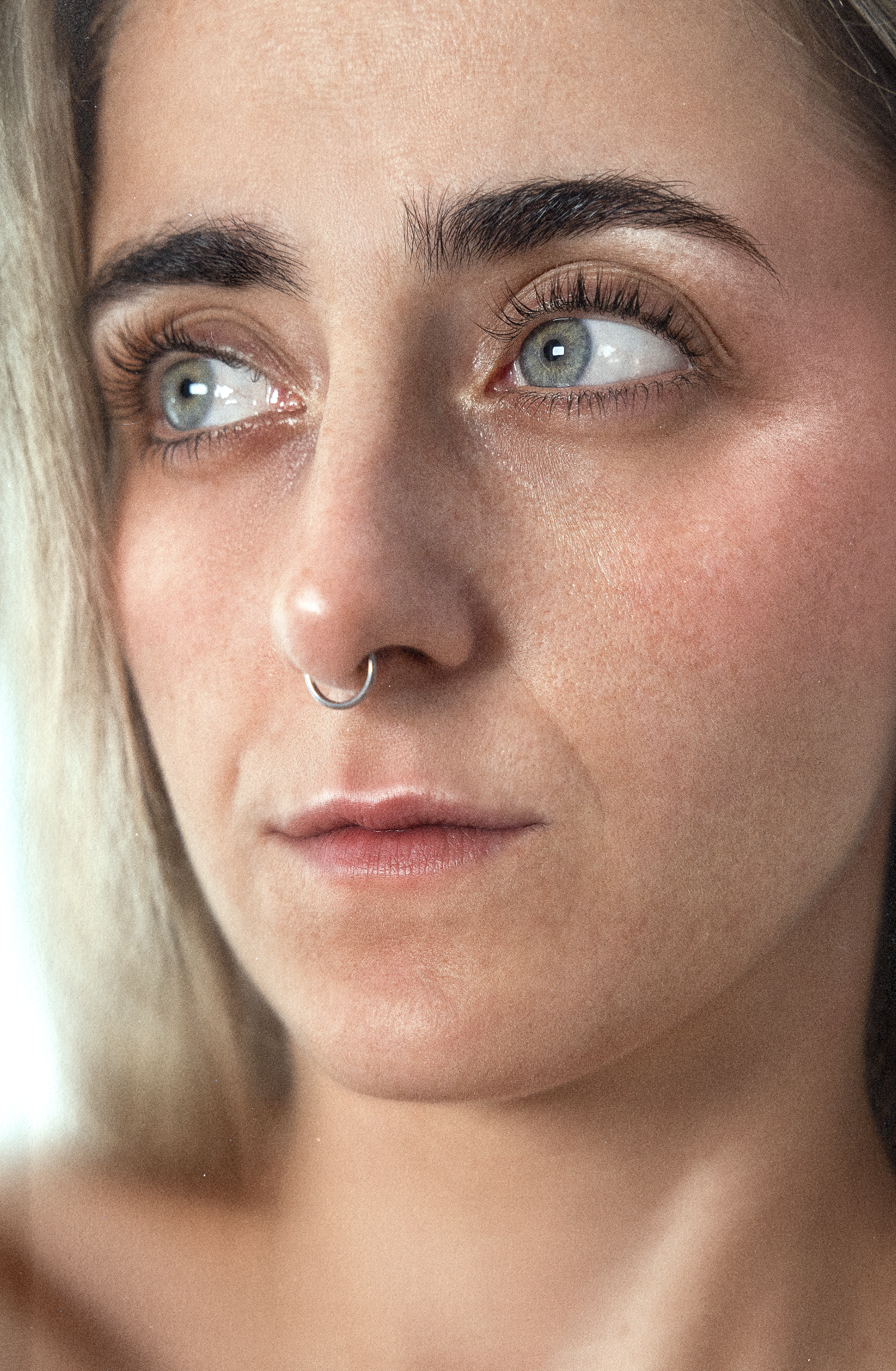 Primer plano de rostro de mujer, enfocado en ojos azules, cejas oscuras y labios suaves, con tono de piel claro y sin maquillaje notable.