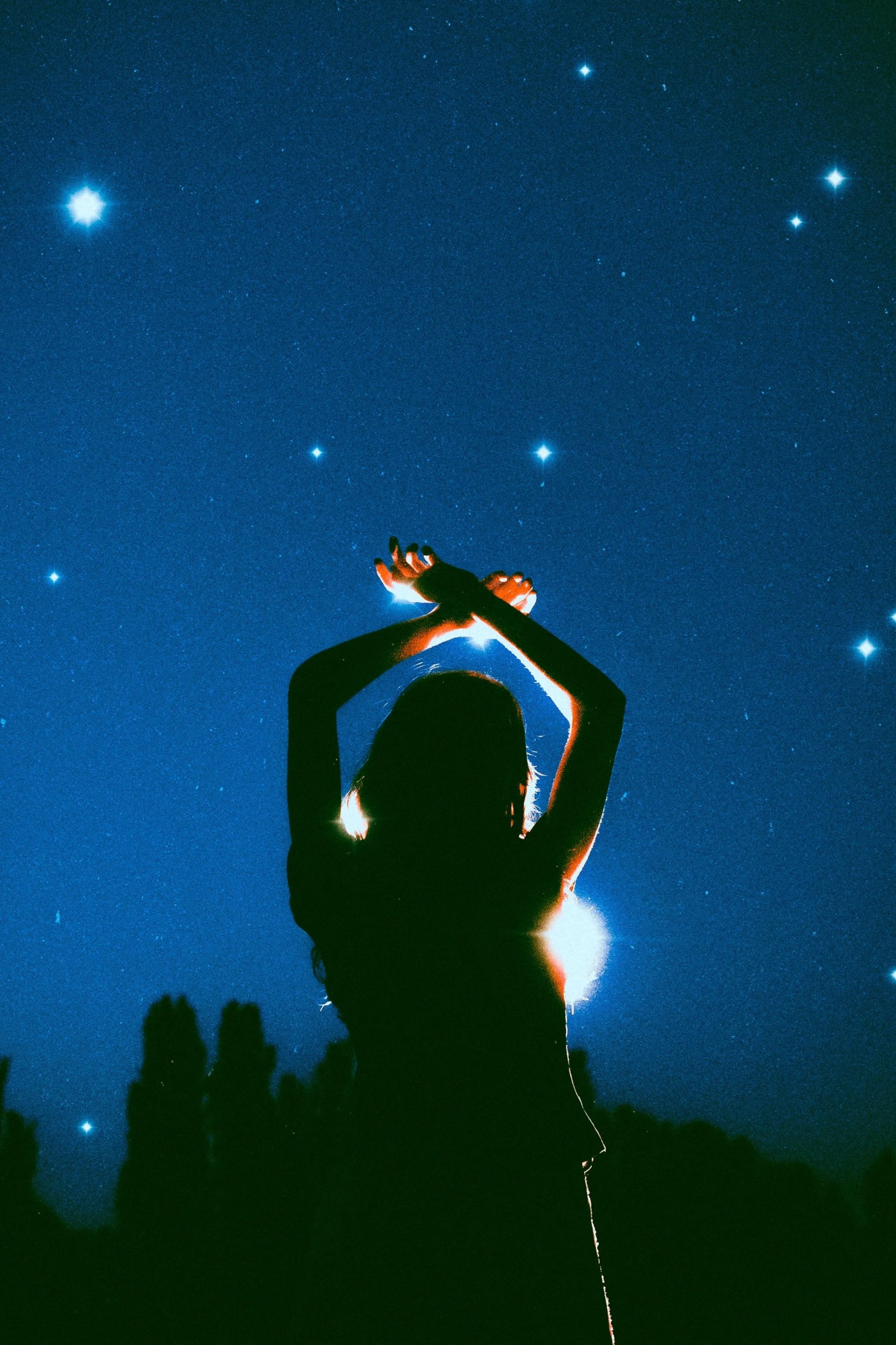 Silueta de una persona de espaldas con brazos levantados frente a un cielo oscuro lleno de estrellas