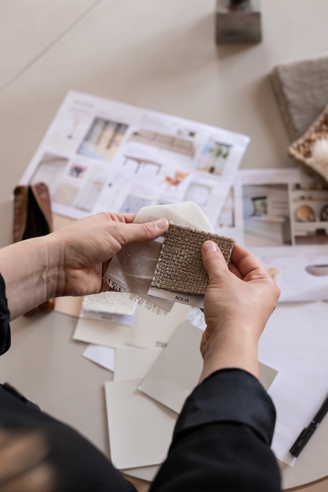 Hænder der holder tekstilprøver op mod hinanden. Der ligger moodboards på bordet i baggrunden og det ser kreativt ud.