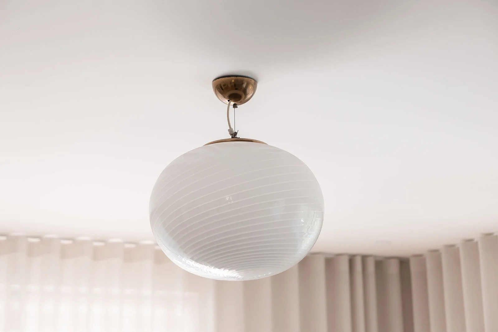 Hvid, rund loftlampe hænger fra en messingfarvet loftbeslag
