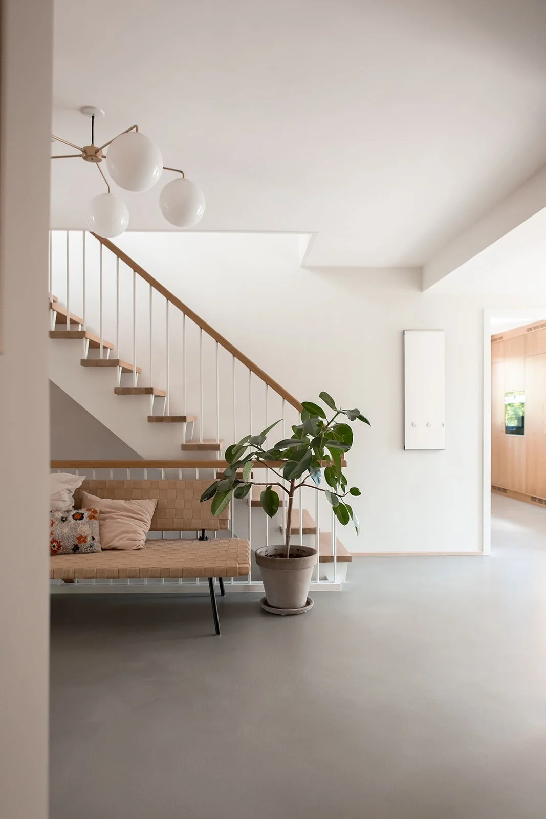 Indendørs stue med trappe, en pæonplante i en vægskål, og en sofa med puder, minimalistisk design, neutral farvepalet, moderne belysning.