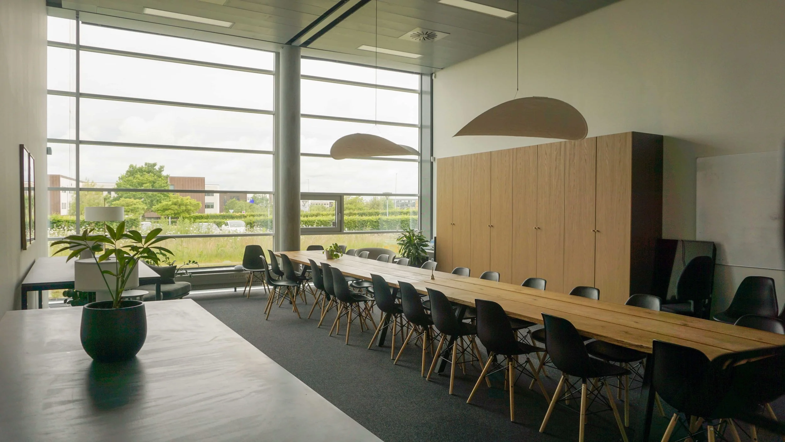 Mødelokale i nordisk stil med langbord i egetræ og eames stole samt new works lamper