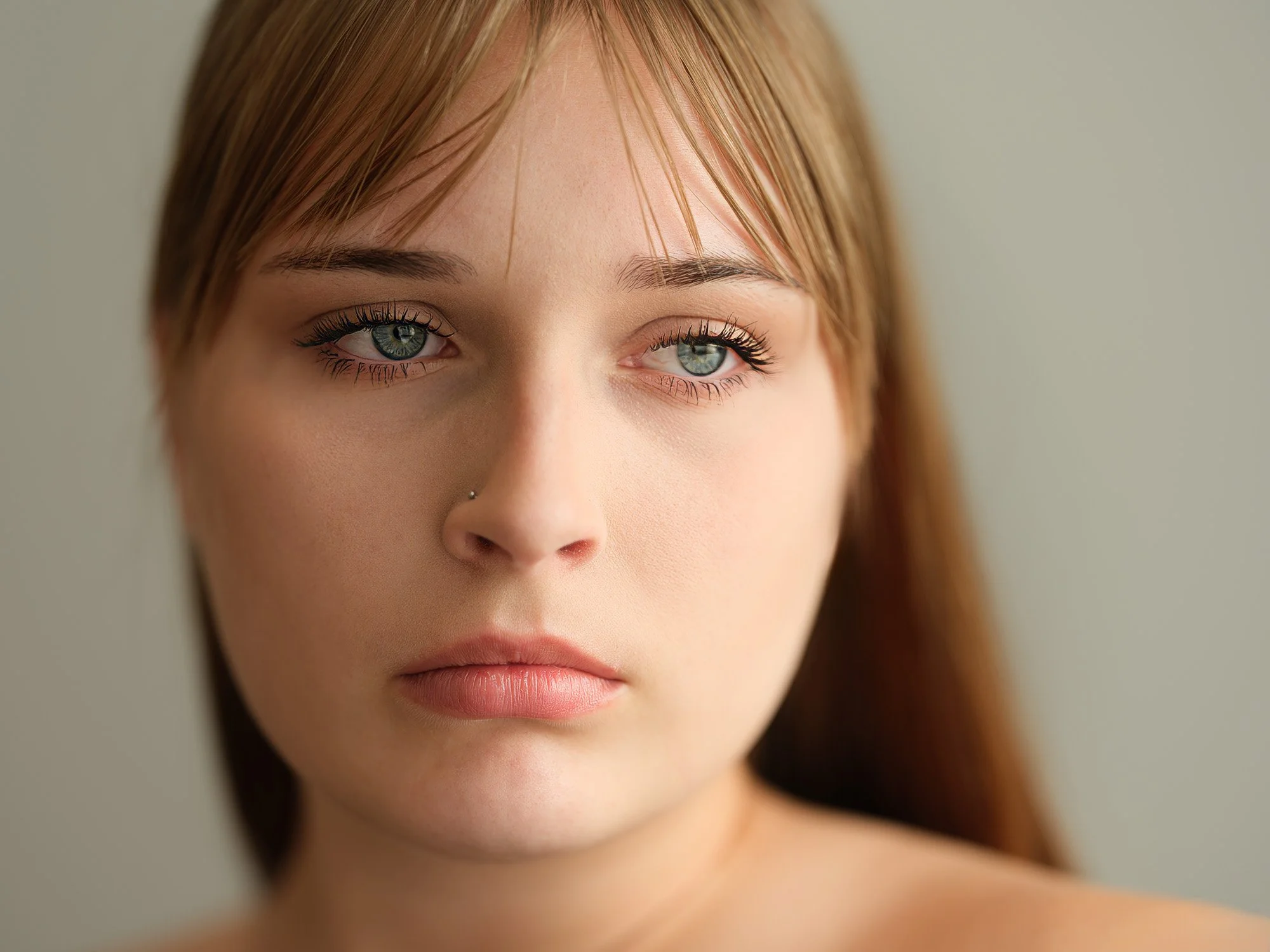 Close-up of a young woman with light skin, blue-green eyes, red hair, and a nose piercing, looking slightly to the side.