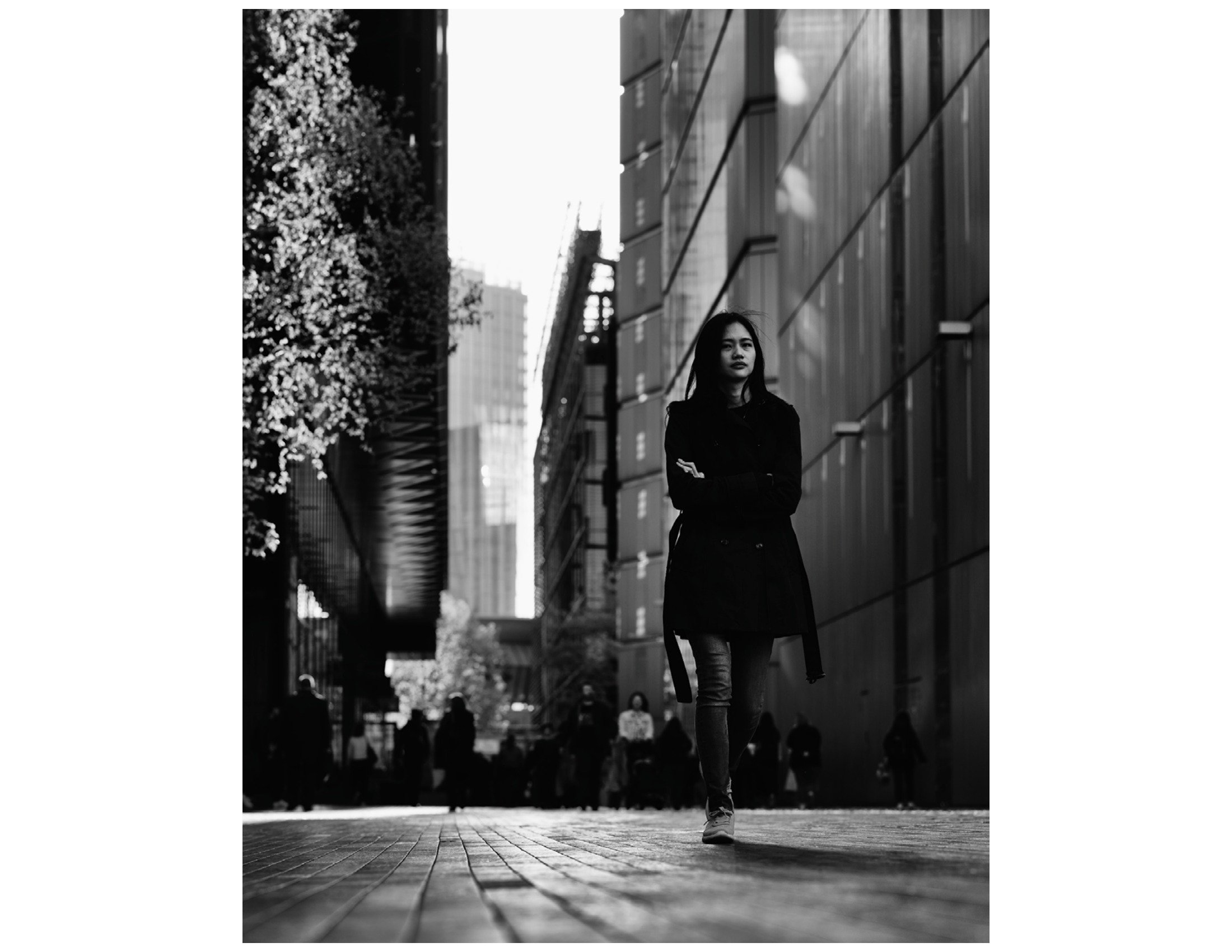 A woman walking on a city street with modern buildings in the background, captured in black and white.