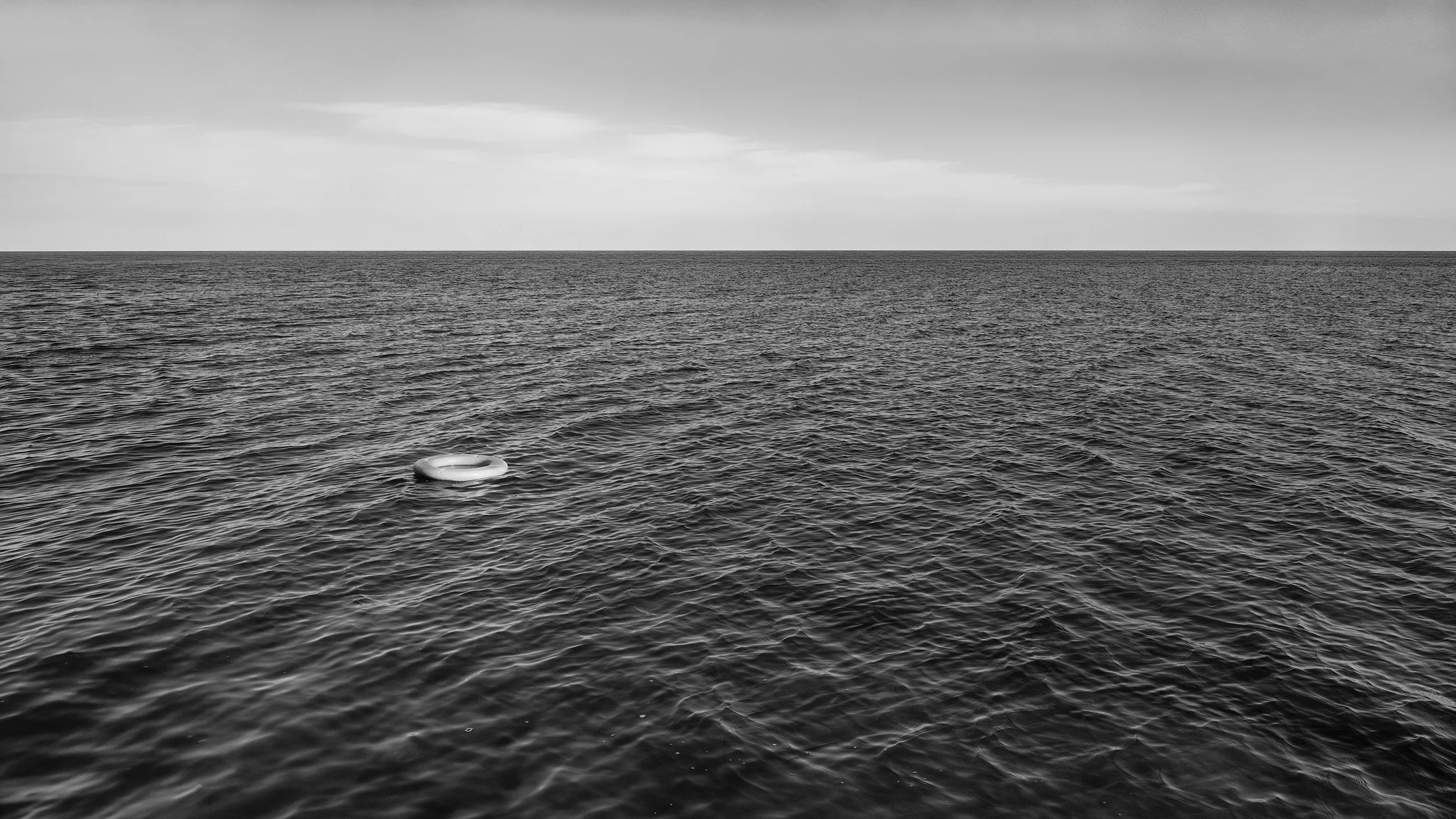 Black and white photo of the ocean with a life preserver floating on the water.