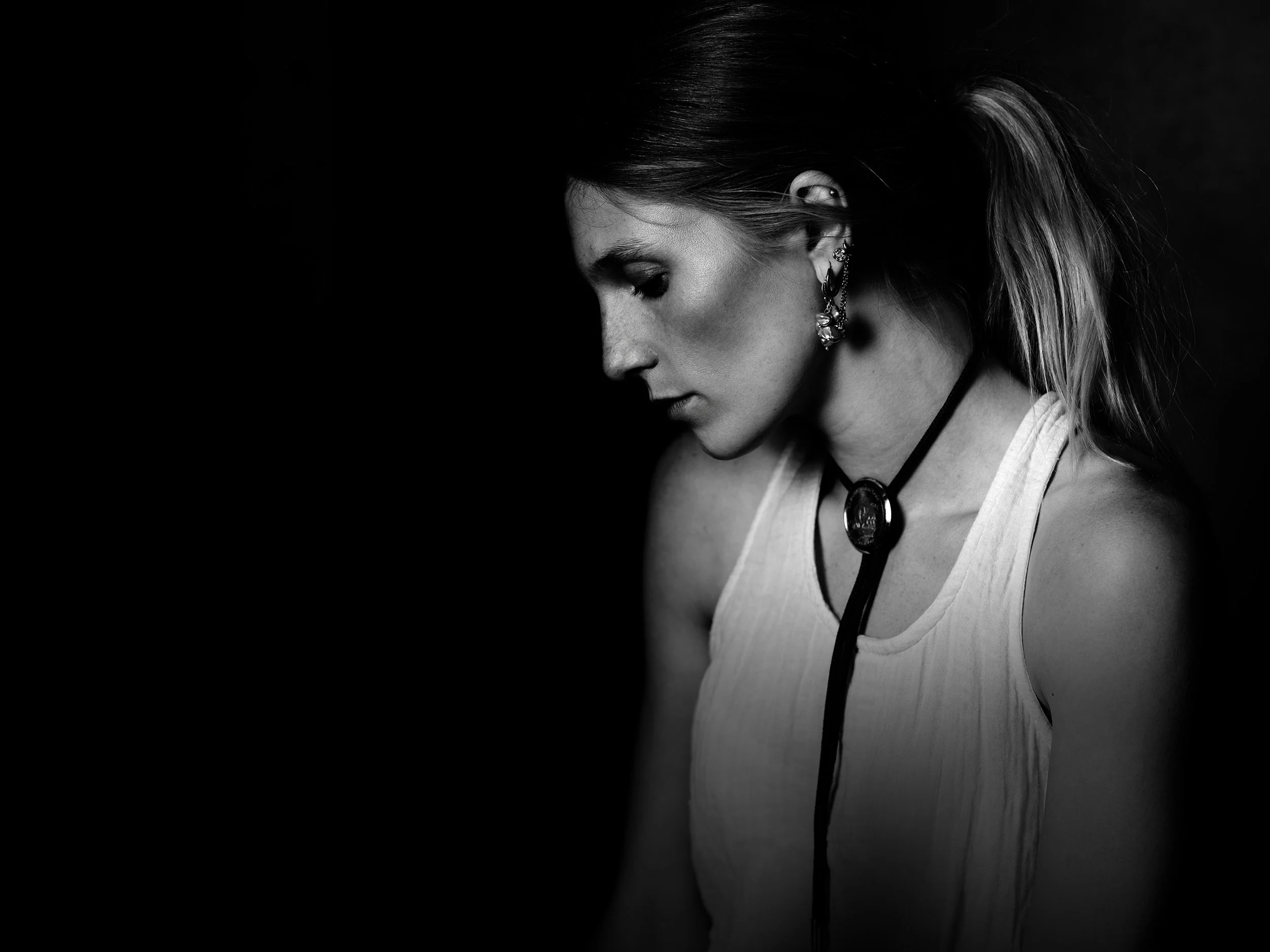 Black and white photograph of a woman with long hair and earrings, looking downward.