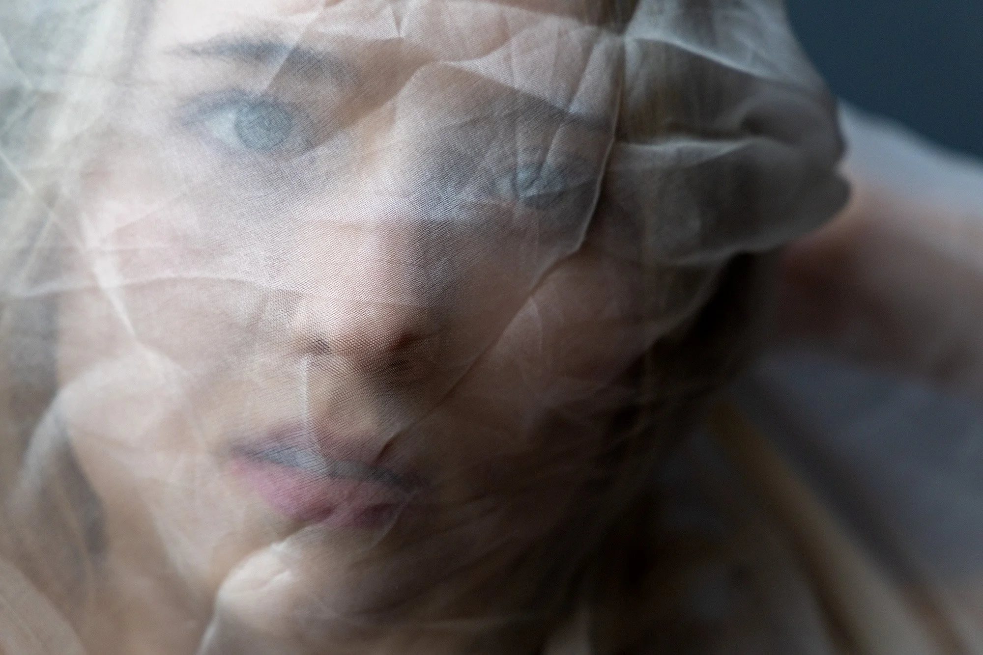 Close-up of a person's face behind a semi-transparent protective mask, with visible eye and lips.