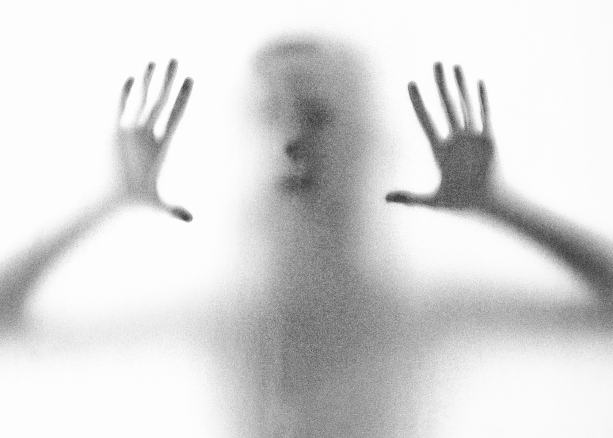 Blurred silhouette of a person behind frosted glass with hands pressed against it.
