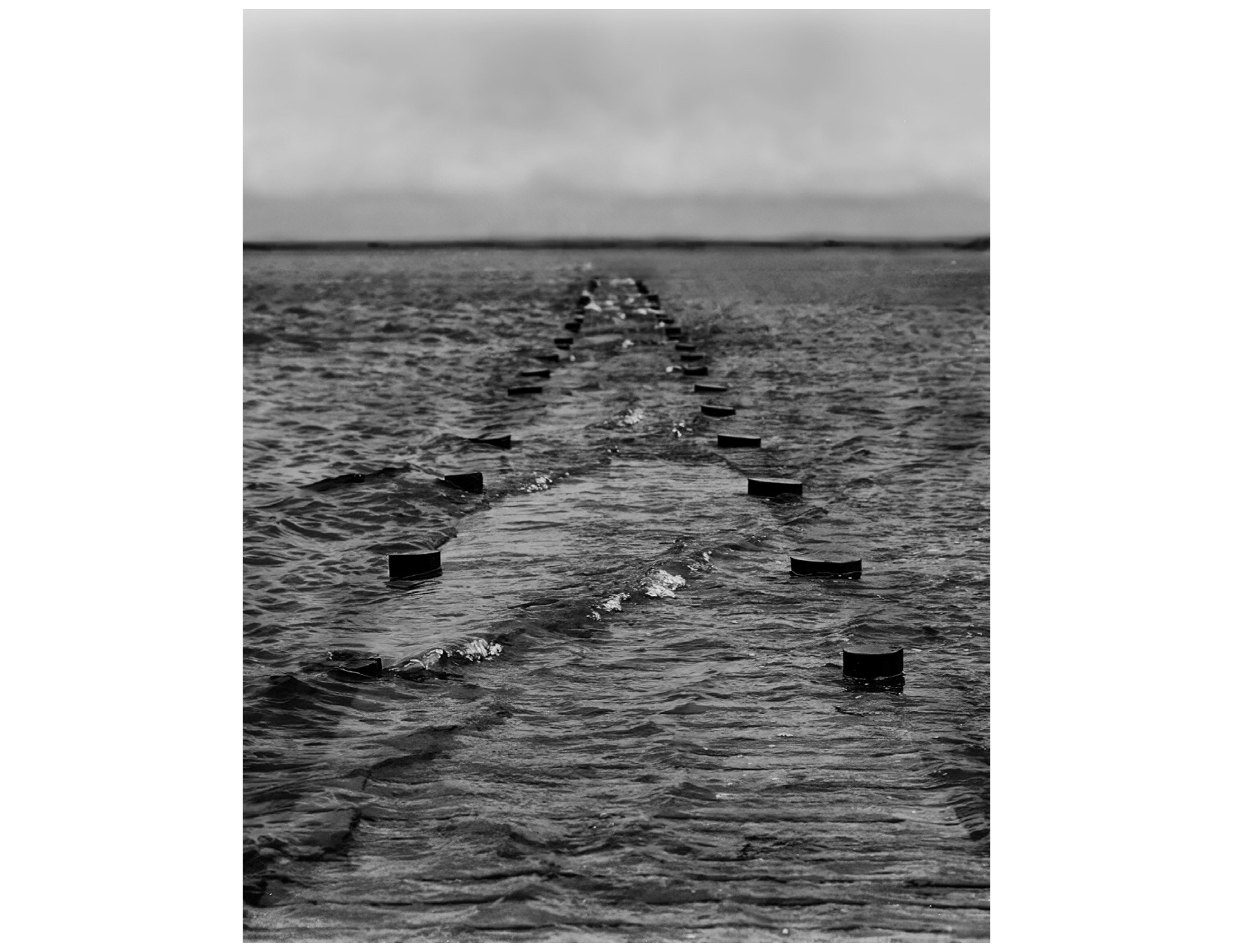 A series of buoys marking a channel in the ocean with an overcast sky.