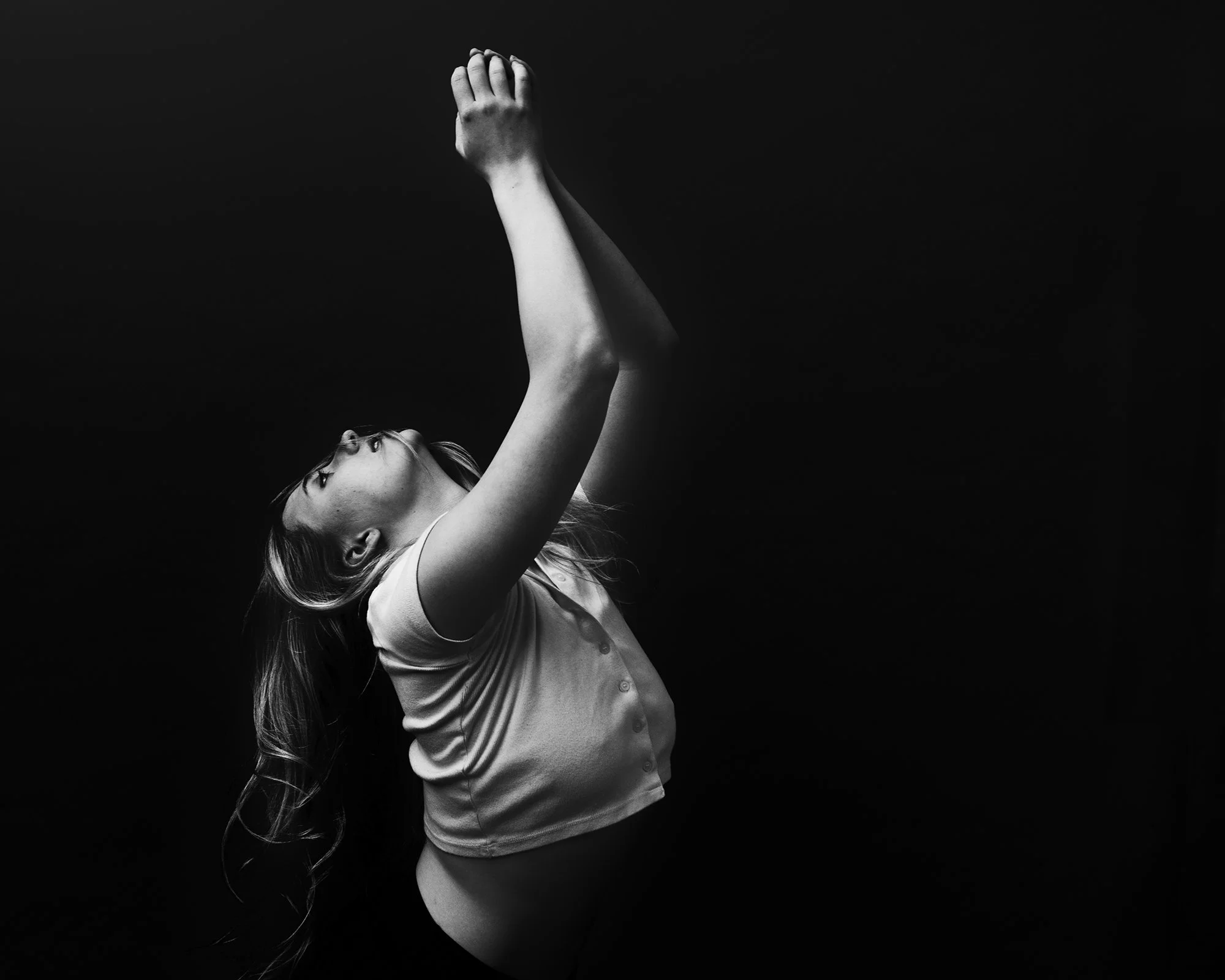 A woman is underwater, floating upward with her head tilted back and eyes closed, with her arm extended above her head, in a black and white photograph.