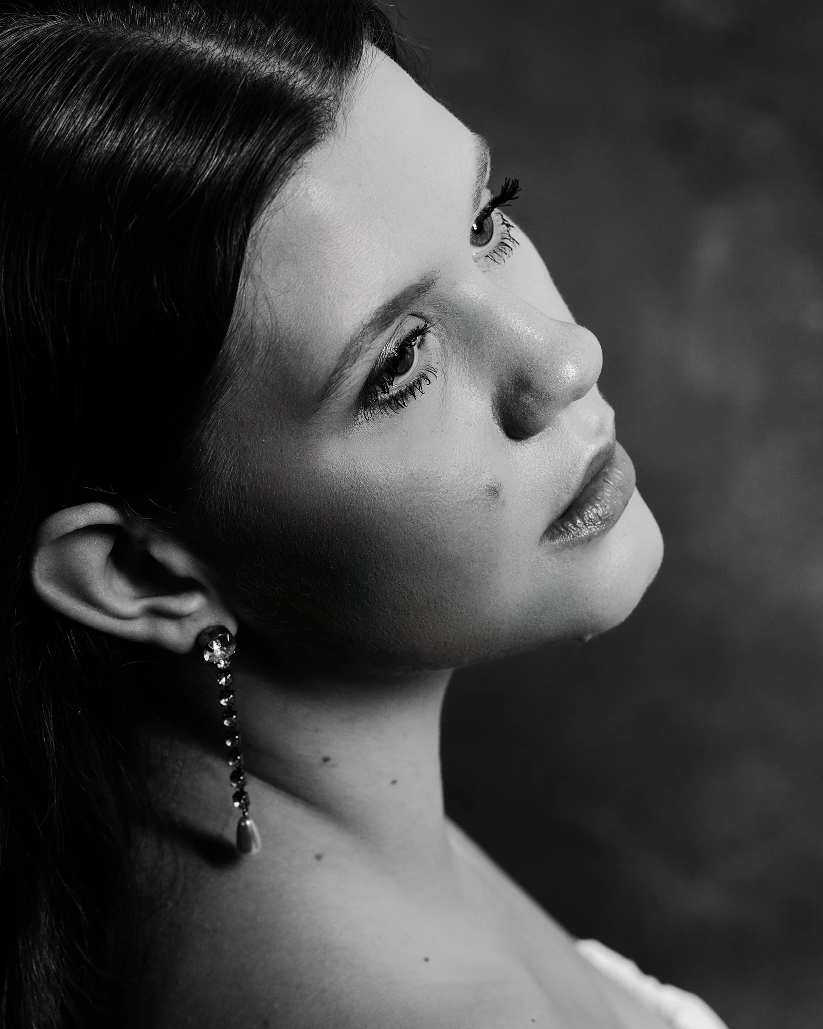 A black and white portrait of a woman with dark hair, wearing an earring, gazing sideways with a serene expression.