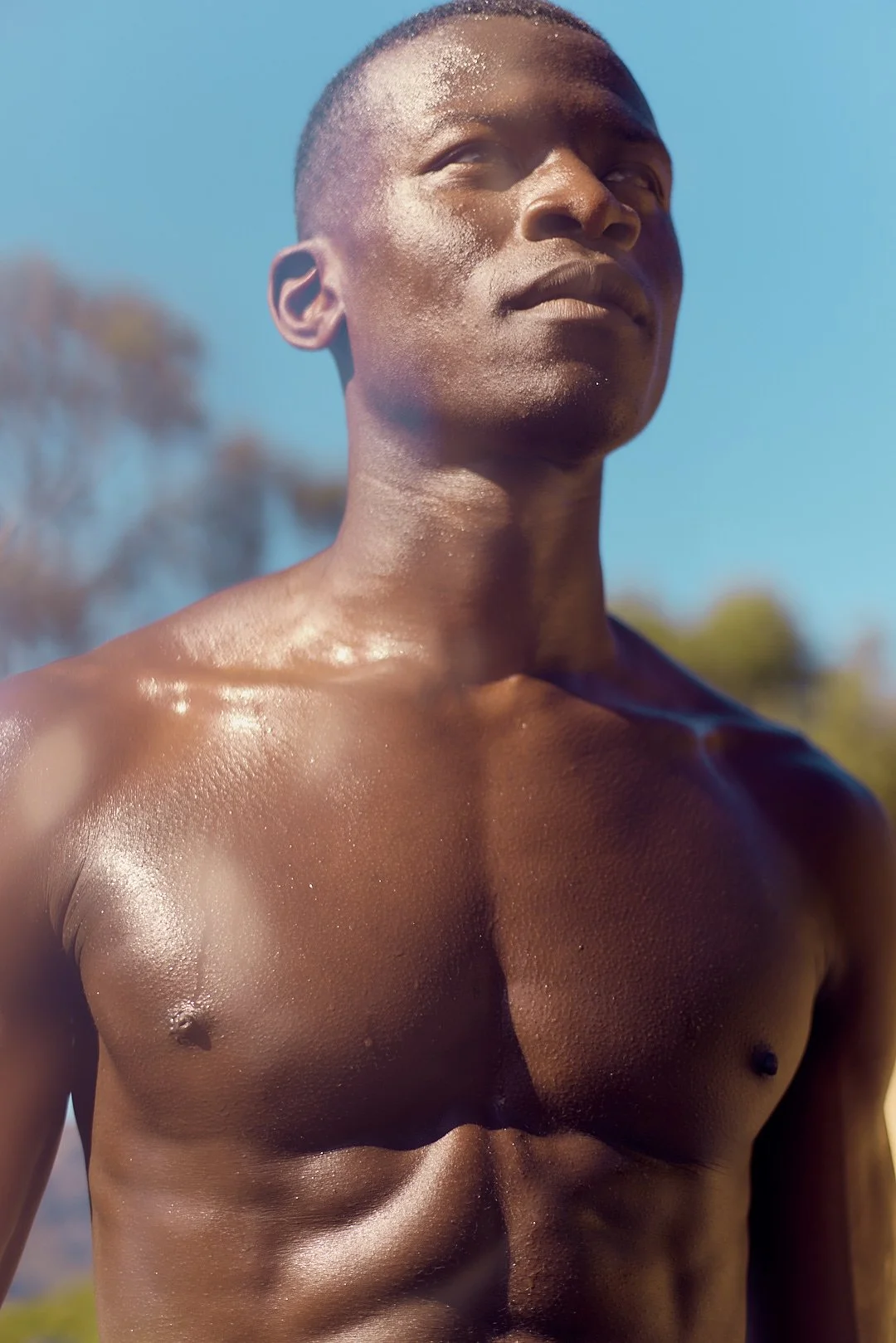 Active lifestyle photography by Justin Munitz - close-up of a shirtless model outdoors, with trees and blue sky in the background.