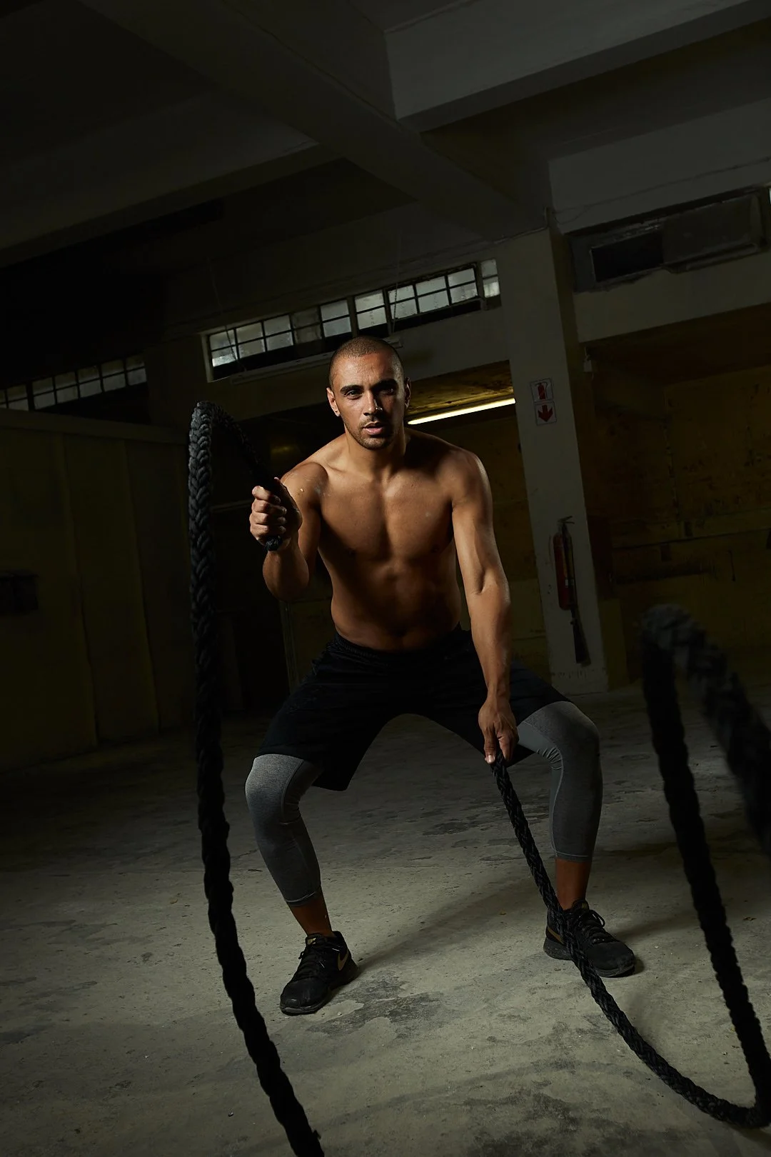 Active lifestyle photography by Justin Munitz . A shirtless model holding battle ropes in a gym with concrete floors.