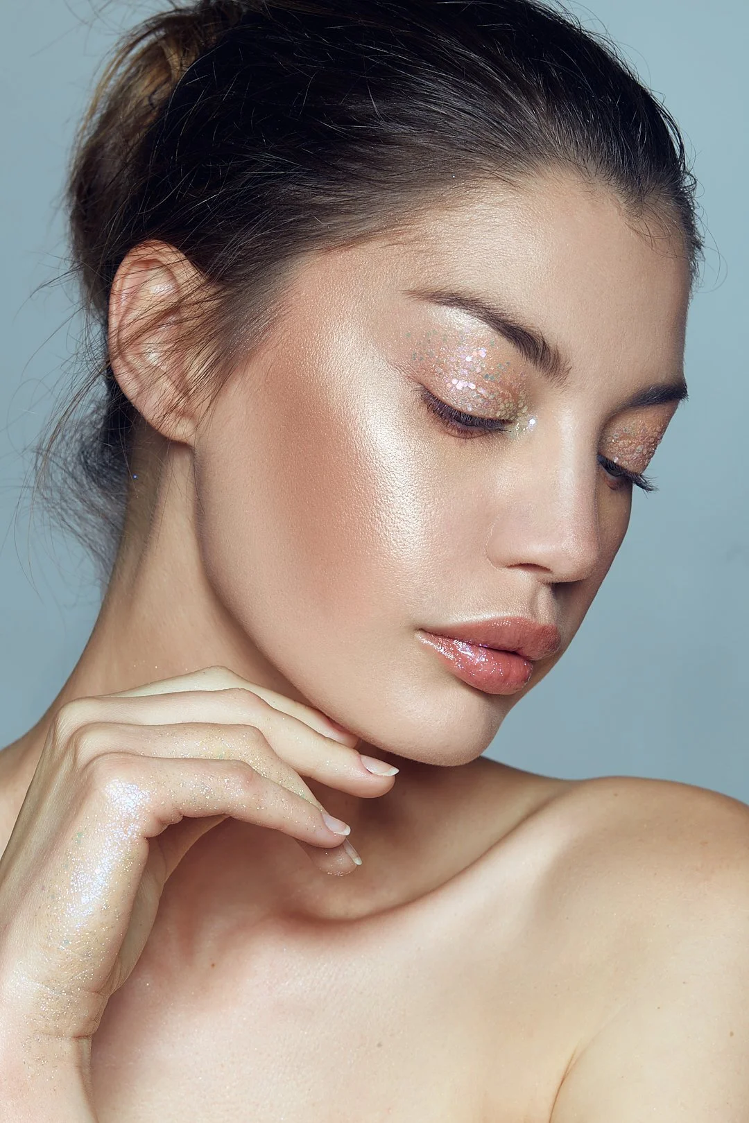 Close-up beauty portrait with glittery eye makeup and glossy lips, touching her chin, photography by Justin Munitz.