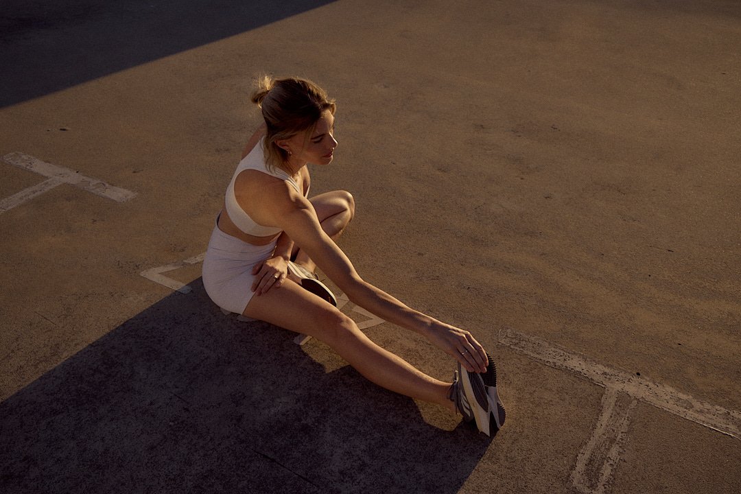 Active lifestyle photography by Justin Munitz — model stretching on a track at sunset.