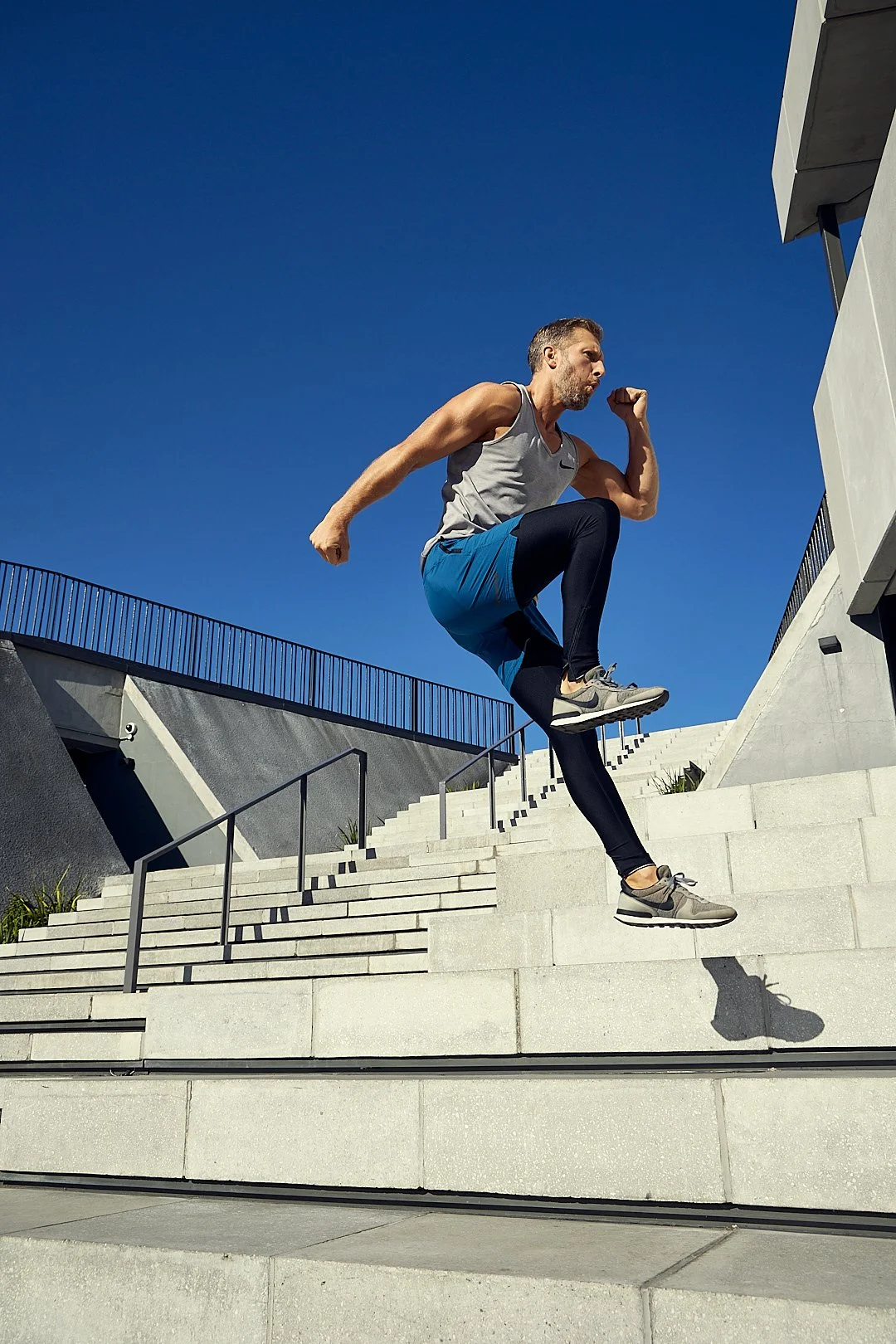 A man wearing workout clothes jumping down stairs outside on a sunny day.