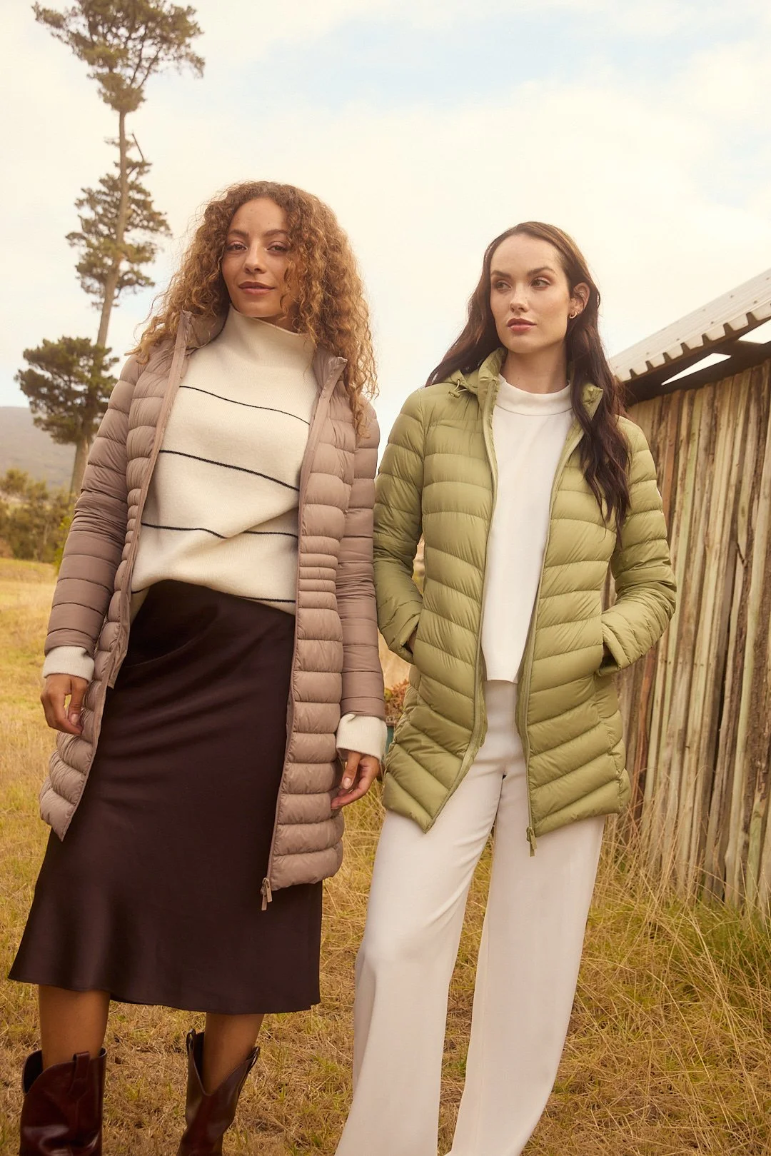 Fashion photography by Justin Munitz — two models wearing puffer jackets, standing outdoors near a wooden fence