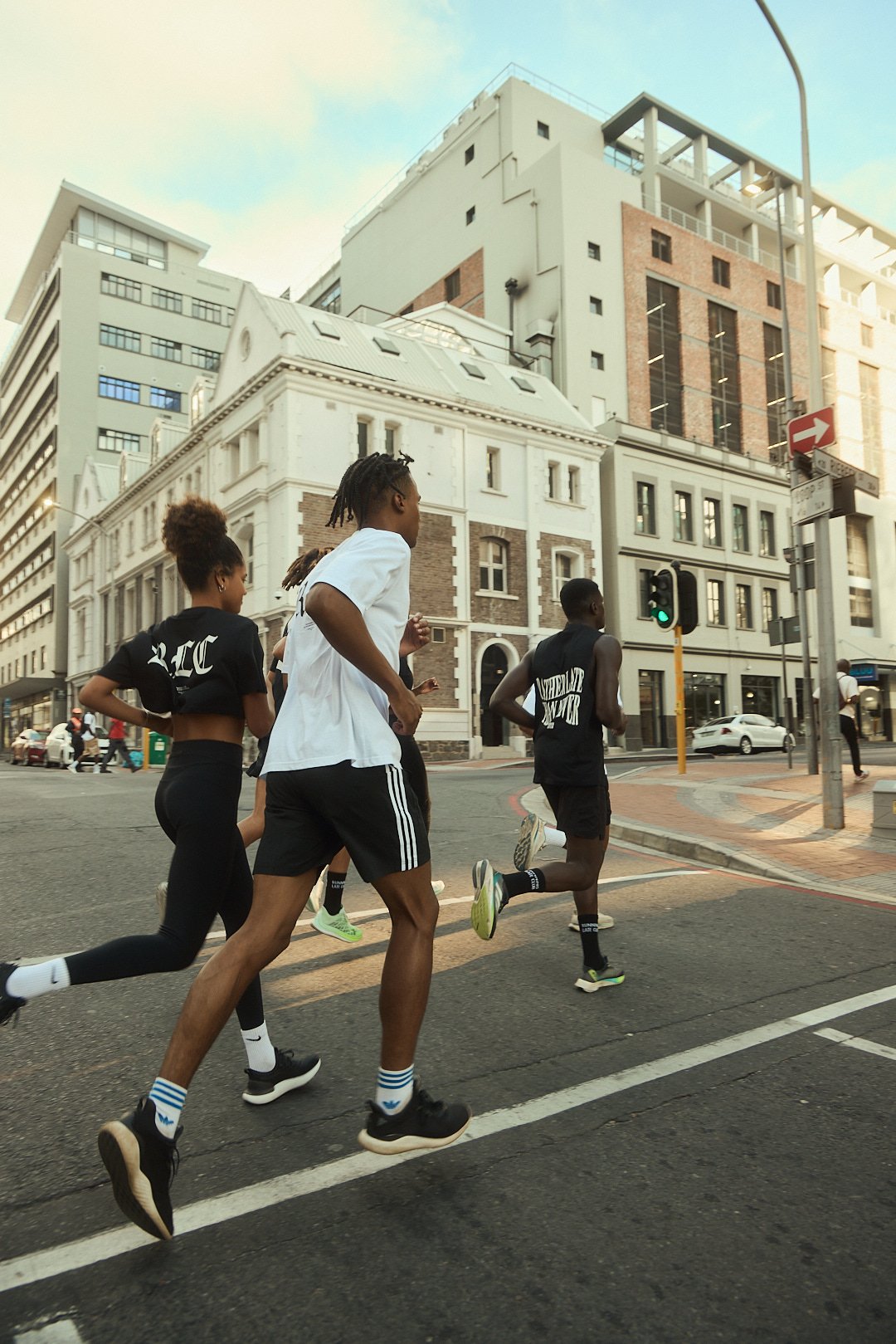 Group of runners participating in a race crossing an intersection in an urban area with tall buildings and traffic signals.