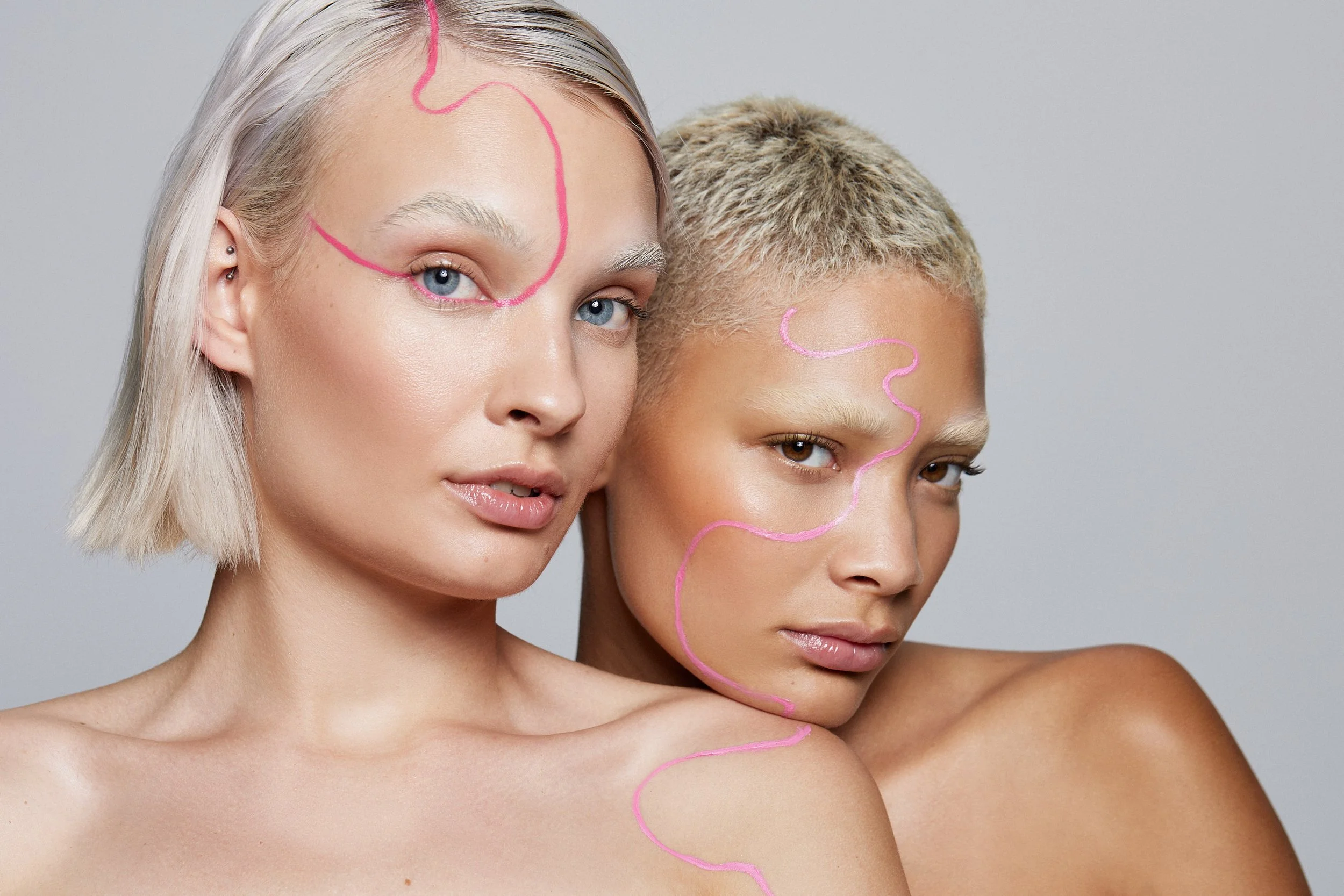 Two models with pink artistic line details drawn on their faces and shoulders, photography by Justin Munitz.