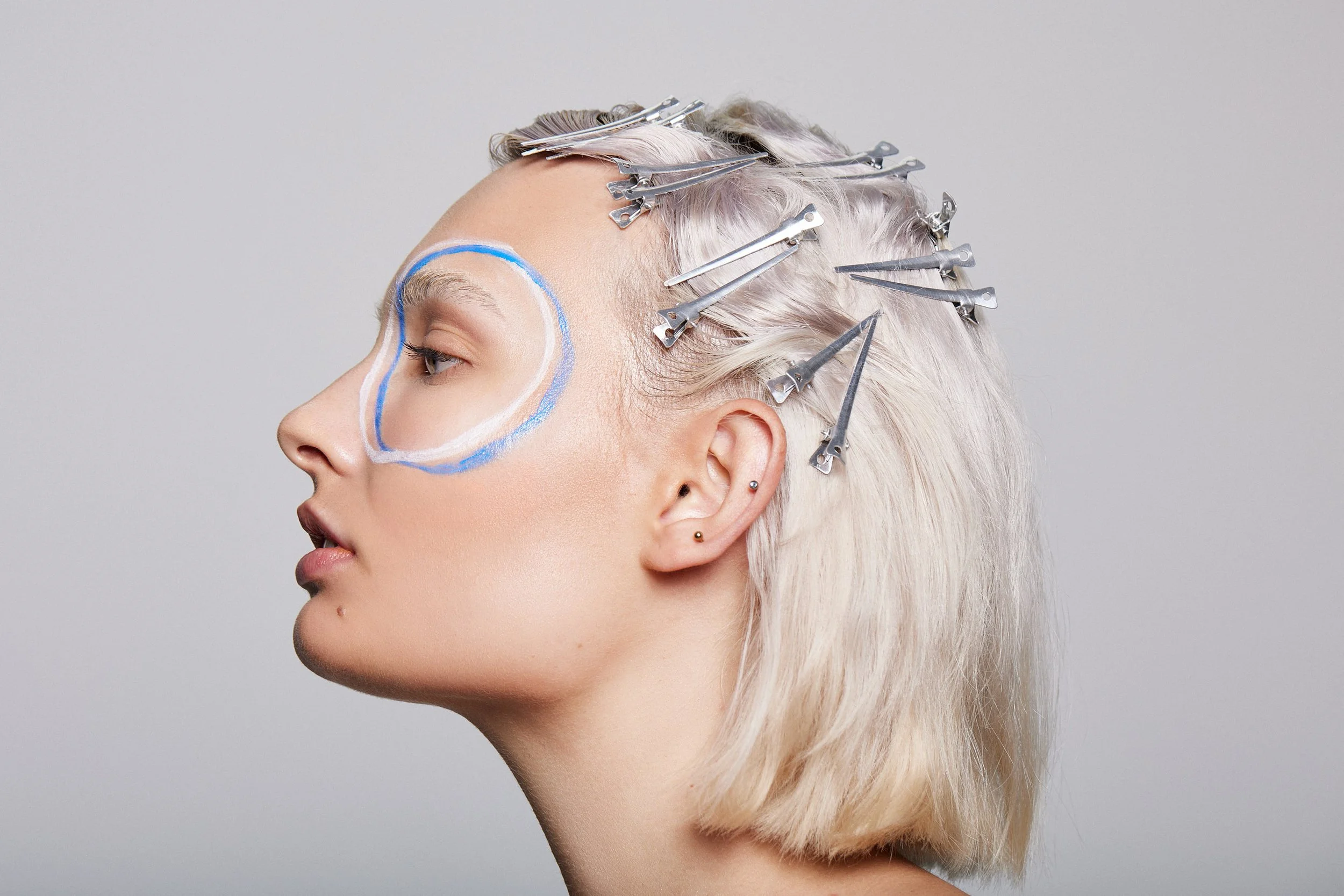 Close-up beauty portrait with silver hair clips and white and blue makeup circles around the eye, photography by Justin Munitz.