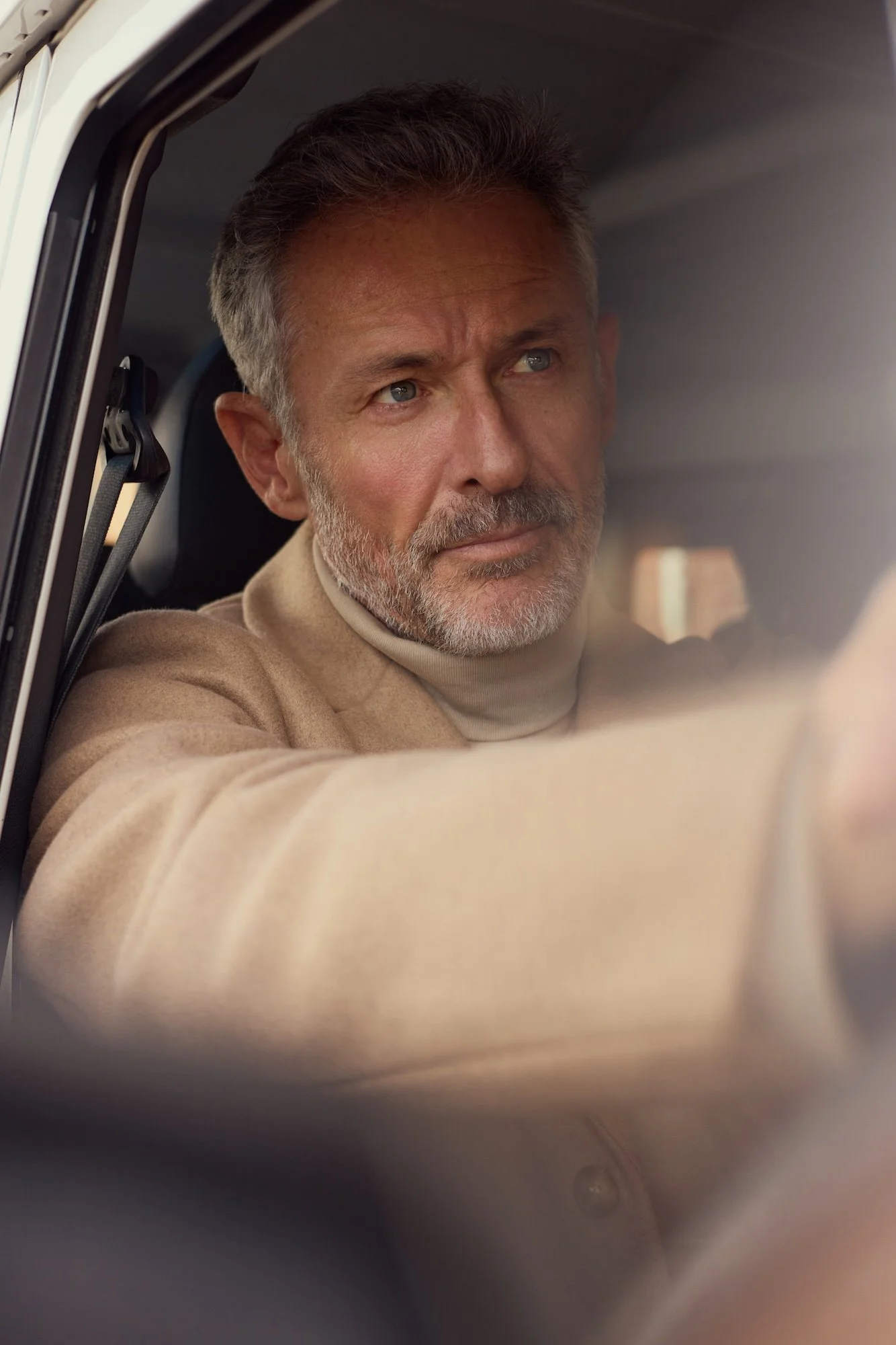 A middle-aged man with gray hair and a beard looking out of a vehicle window.