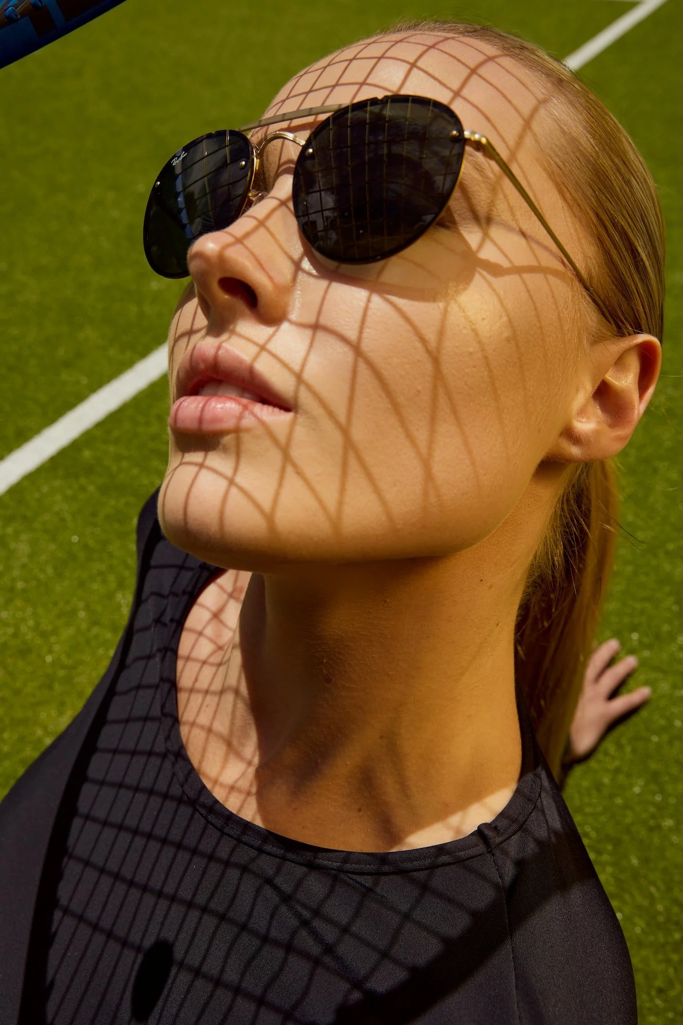 Active lifestyle photography by Justin Munitz - close-up of a model wearing sunglasses, lying on a tennis court.