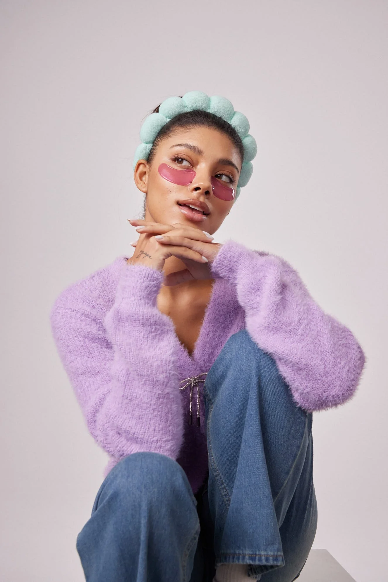 Model wearing pink eye patches, a pom-pom headband, and a purple sweater, photography by Justin Munitz.
