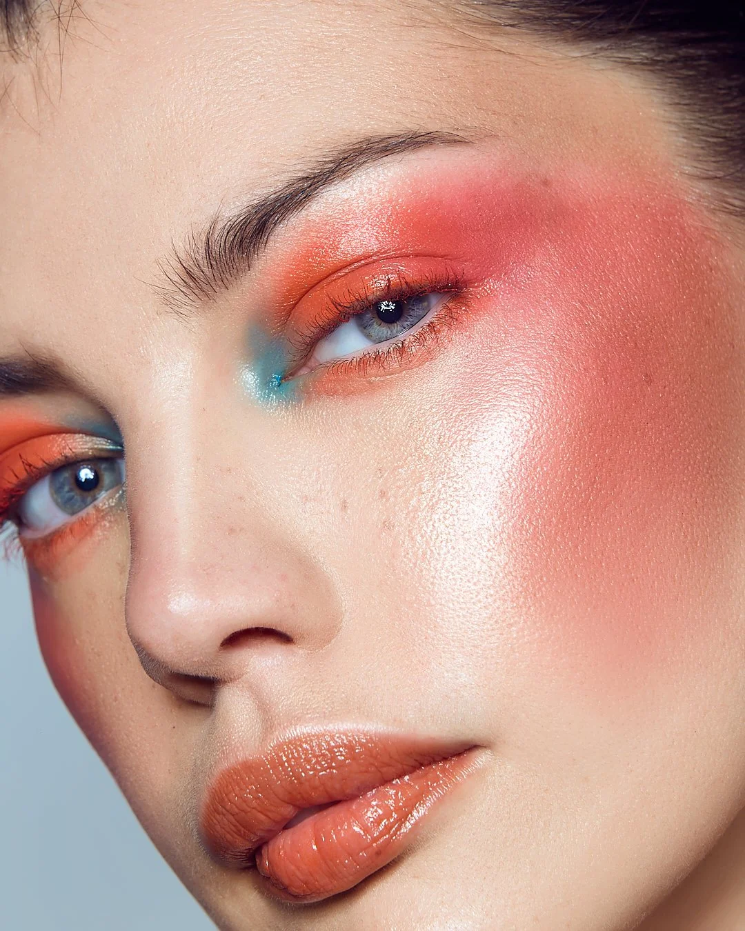 Close-up beauty portrait with peach and pink eyeshadow, blue accents, and glossy peach lipstick, photography by Justin Munitz.