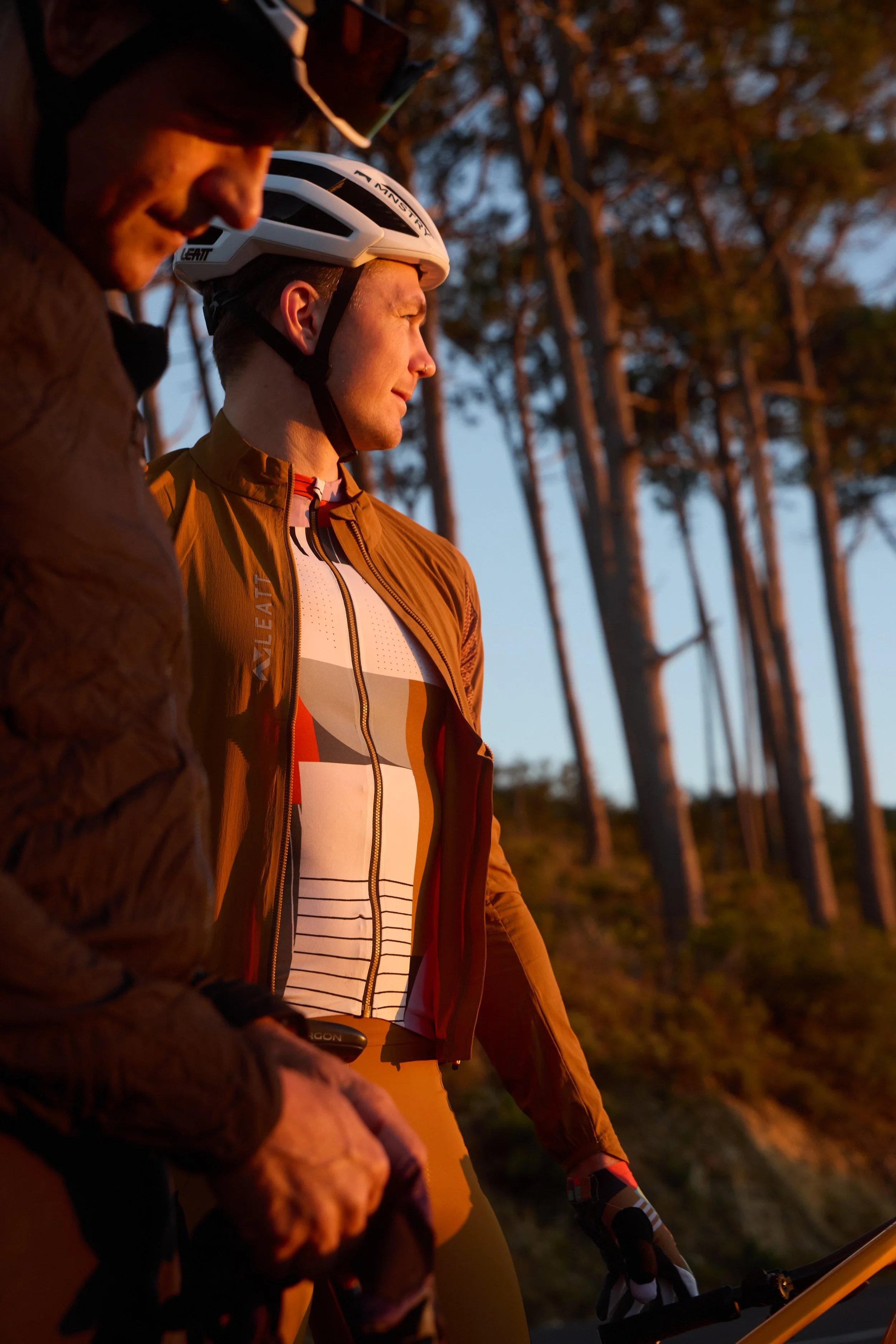 Active lifestyle photography by Justin Munitz - two models with helmets and cycling gear, standing outdoors during sunset.