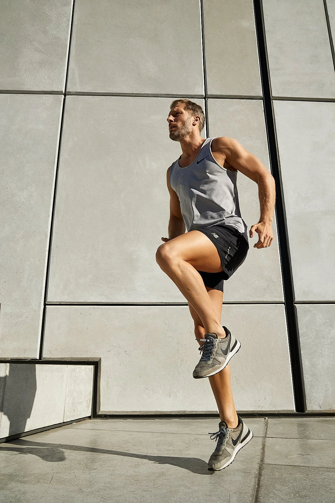 Active lifestyle photography by Justin Munitz - model in athletic clothing jumping in front of a modern building exterior.