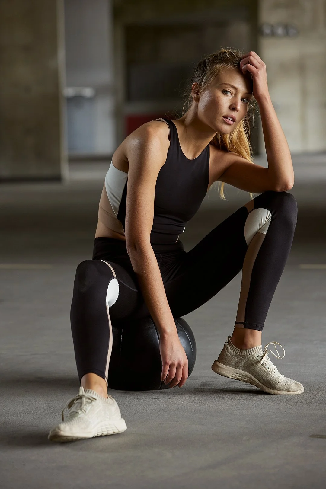 Active lifestyle photography by Justin Munitz — model in workout clothes seated on the floor in a gym, resting an arm on a medicine ball.