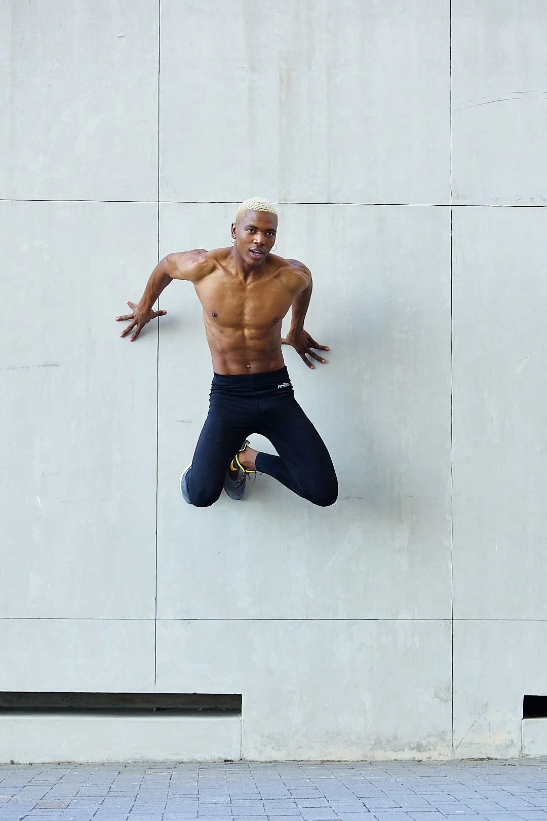 Active lifestyle photography by Justin Munitz — shirtless model jumping against  a wall, wearing black pants and running shoes.